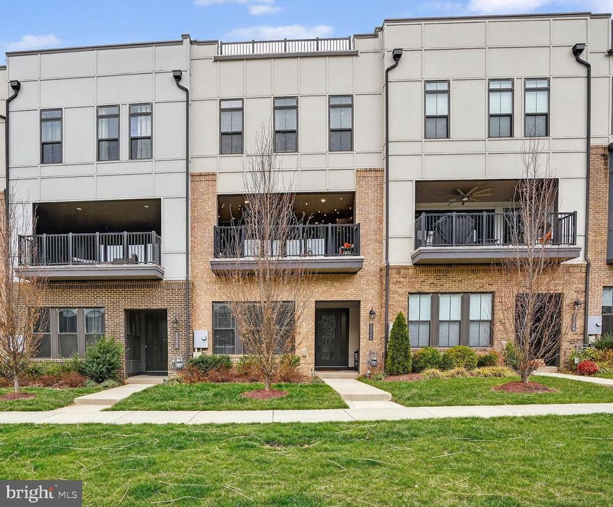 If you’re looking for a home that effortlessly blends style, comfort, and a vibrant community lifestyle, 23048 Lavallette Square delivers on every level. This beautifully appointed 3 Bedroom, 2 Full Bathroom, and 2 Half Bathroom townhome is tucked into the heart of Brambleton, one of Loudoun County’s most desirable Master Planned communities, where convenience and contemporary charm come together seamlessly.

From the moment you arrive, the stately brick façade and covered front porch set the tone for what’s inside—thoughtful design, quality finishes, and spaces that truly feel like home. Step through the front door and you’re greeted by a bright, open Foyer with soaring ceilings, warm LVP flooring, and a welcoming sense of space. The lower level offers a flexible living area that easily adapts to your lifestyle, whether it’s hosting friends, gathering family for a cozy movie night, or simply unwinding at the end of the day. A built-in wet bar with granite counters and custom cabinetry adds a fun, elevated touch that makes entertaining here feel effortless.

The main level is where this home really shines. Designed to impress, the Kitchen is the centerpiece—expansive, inviting, and designed for gathering. A dramatic 14-foot island anchors the space, offering plenty of room for cooking, casual dining, or simply hanging out while meals come together. With granite countertops, stainless steel appliances, rich cabinetry, and sleek lighting, it strikes the perfect balance between functional and stylish. The open flow into the Dining and Family Rooms creates a natural rhythm for everyday living and hosting alike, while oversized windows fill the space with natural light.

Just off the main living area, the covered deck becomes an extension of the home itself. Step outside to the private, covered balcony overlooking common green space, where a retractable privacy screen, string lighting, and ample room for seating create an inviting outdoor retreat. Whether it’s morning coffee, evening cocktails, or weekend lounging, this private outdoor space extends your living area beautifully and offers a quiet retreat from the day-to-day hustle and bustle.

Upstairs, the Primary Suite feels like a true sanctuary. Generous in size and filled with light, it features a comfortable sitting area and a walk-in closet that offers exceptional storage and organization. The En-Suite Bathroom elevates daily routines with dual vanities, beautiful tilework, and a spacious walk-in shower designed with both style and comfort in mind. Two additional Bedrooms provide flexibility for guests, family, or a home office, all complemented by a well-designed hall Bathroom and the convenience of a coveted upper-level Laundry Room.

Additional features include a two-car Garage with built-in shelving and a driveway for added parking.

Living in Brambleton means more than just owning a beautiful home—it’s about enjoying a connected, amenity-rich lifestyle. From 18 miles of scenic trails and community events to pools, parks, and the nearby town center filled with dining, shopping, and entertainment, everything you need is right at your fingertips. Add in easy access to major commuter routes and the Silver Line Metro, and you have a location that truly works for both daily life and long-term convenience.

At 23048 Lavallette Square, you’re not just finding a place to live—you’re finding a place to belong.