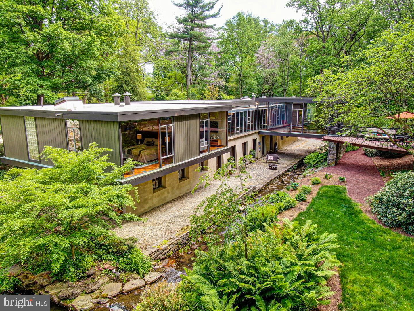 Extraordinary and iconic mid-century modern home , built in the International Style in 1958-59, and designed by the firm of Montgomery and Bishop - Architects. Listed on the Philadelphia Register of Historic Places in 2011 (p.76 of 259), this "glass" house epitomizes the philosophy of "organic architecture" in which structures were designed in harmony with nature. One of the home's architects, Robert F. Bishop, worked with Frank Loyd Wright at Taliesen in the 30's. The house is sited below the road into a hillside in the front and cantilevered in the back over a stream. Seen from the drone footage, the house consists of three large rectangular spaces: the main living area, the family bedrooms, and, originally, a third wing designed as a mother-in-law suite. The two family areas are joined by a long corridor with floor-to-ceiling plate glass windows, looking out over the creek and the adjacent hillside. From the front entrance, which is recessed between two wings, the house opens to a light-filled, slate floored entryway, separated from the living room by a floating rectangle that houses three closets. Turning left, from the foyer, you enter a wing comprised of four bedrooms and two full baths. One of the baths is a jack-n-jill. The other is accessed from the hallway. Turning right out of the foyer, you enter the main family living space with grand, high-ceilinged living room; an open kitchen; and adjoining dining room. The originally designed "mother-in-law suite" now serves as the master wing, made up of a serene living room with second wood-burning fireplace, the master bedroom, master bath, dressing room, and private office area. There are two staircases to the lower level which offers more desirable and flexible living space. One comes off the master wing and enters into a studio space, currently used for music. From the music room, you walk into a lounge and exercise area equal to a five-star spa. A series french doors give you easy access to the outdoors from the lower level. A beautiful laundry room, a capacious "work room" , two more bedrooms and two more baths complete the lower level. The accompanying photos hardly capture the beautiful outside space, but, certainly words won't accomplish it.