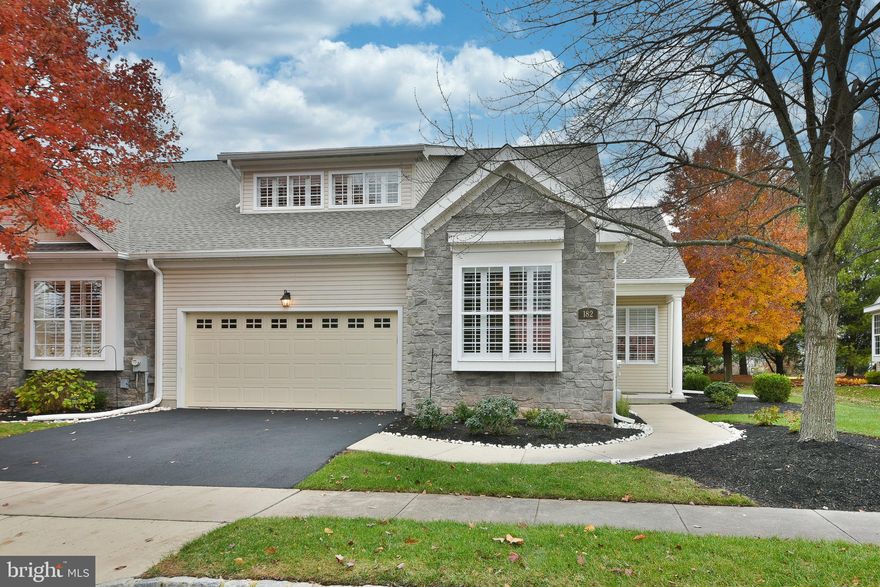 Located in the highly sought-after 55+ Courtyards at Collegeville community, 182 Lattuce Lane is a beautiful stone and siding end unit , and as a former model home, offers premium upgrades not found in other units. Thoughtfully designed for both comfort and convenience, this home showcases enhanced finishes and details that set it apart within the community. You are welcomed by well-maintained landscaping and a charming covered front porch that sets the tone for what awaits inside. Step into the foyer, where hardwood flooring creates a warm and inviting first impression. To the right, the formal dining room features a chandelier, double crown molding, elegant millwork, and windows adorned with custom plantation shutters, making it an ideal space for both everyday meals and special gatherings. Continue into the eat-in kitchen, which offers ample counter and cabinet space, newer appliances, Corian countertops, tile flooring, double sink, and a peninsula with barstool seating for casual dining or entertaining. There is also an opening through to the living room which makes interacting with family and guests a breeze. The kitchen flows seamlessly into the Florida room, a relaxing retreat that also features custom plantation shutters, ceiling fan, new skylights, and overlooks the outdoor living space. French doors lead to the brick patio, providing the perfect tree lined setting  to enjoy your morning coffee or dine al fresco during the warmer months. The main level offers two well-appointed bedrooms, providing the ease and convenience of one-floor living. The spacious owner’s suite is privately located at the rear of the home and features a tray ceiling with crown molding, ceiling fan, and a generous walk-in closet with custom shelving. The en suite bath is highlighted by a custom double shower with overhead lighting added in 2020, tile flooring, and a vanity designed for both style and functionality. An additional bedroom with new hardwood flooring is situated at the front of the home and is served by a full hall bathroom, making it ideal for guests or a home office. A conveniently located laundry room completes the main floor and allows access to the two car garage with garage door opener. A valuable bonus awaits upstairs in the expansive loft area, offering flexible space that can easily serve as a home office, media room, craft area, or comfortable accommodations for additional guests. This inviting space features recessed lighting, a ceiling fan, and a closet for added storage. The true highlight is the convenience of an additional half bath, along with a wet bar area complete with a mini refrigerator and microwave—perfect for entertaining or creating a private retreat. A full unfinished basement is perfect for all of your storage needs. 
Notable upgrades include- New roof  (2025), new skylights in Florida room (2025), new HVAC (2023), owner’s bath double shower (2020), custom Plantation shutters throughout most of the home, and new hardwood flooring in second bedroom (2025). Ideally situated with easy access to Route 422, Ridge Pike, and Germantown Pike, the property provides effortless connectivity to everyday necessities and leisure destinations. Enjoy close proximity to grocery stores, shopping, and dining in Skippack and Providence Town Center, as well as the local library, nearby parks, and scenic walking trails. This exceptional home combines low-maintenance living with an unbeatable location in one of Collegeville’s most desirable active adult communities. ****Showings start on 1/3/2026 at the Open House!****