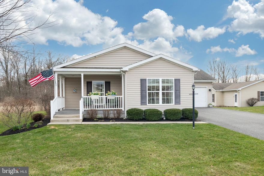 Welcome to this beautifully maintained home in the sought-after 55+ community of Spring Valley Village. Originally the community’s model home, this residence offers exceptional upgrades, thoughtful design, and one of the most desirable lots in the neighborhood. From the moment you arrive, the home’s curb appeal stands out with attractive landscaping and a charming covered front porch with custom vinyl railings—an inviting place to relax and greet neighbors. Step through the decorative leaded-glass front door into a welcoming foyer with a spacious coat closet. The living room flows seamlessly into the heart of the home—an expansive kitchen designed for both everyday living and entertaining. Rich raised-panel cherry cabinetry with upgraded soft-close features is complemented by a newer countertop, tile backsplash, updated sinks, and the convenience of gas cooking. Additional highlights include a large center island with drawer storage and pendant lighting, built-in desk area, glass-front accent cabinets, pantry, wine rack, double wall ovens, smooth-top range, double pull-out trash storage, and generous recessed lighting. The adjoining dining area provides access to the rear deck and opens to the bright morning (family) room, where walls of windows fill the space with natural light. A beautiful electric fireplace with heater and flame ambiance creates a cozy focal point for the room, making it an inviting place to relax in any season. From here and from the rear deck, you’ll enjoy peaceful views of the community’s green space, offering the feeling of a private nature setting just beyond your backyard. The home features two generously sized bedrooms, including a spacious primary suite with an oversized step-in tiled shower and a double-bowl vanity set in an elegant antique-glazed cabinet. The second bedroom is currently used as a home office and includes a custom murphy bed, providing flexible space that easily accommodates overnight guests. A hall bath, with tub and shower, completes the bedroom area. Since purchasing the home, the current owners have added beautiful hardwood flooring, enhancing the warmth and elegance of the living spaces. For additional peace of mind, the heater was replaced in February 2025. A spacious laundry and utility room with abundant cabinetry leads directly to the over-sized two-car garage, which also features pull-down attic steps providing convenient access to additional storage space above. Outside, the rear deck is the perfect place to unwind while enjoying the tranquil setting and open green space behind the home. An exterior outlet has also been installed for convenient RV charging. If you are seeking a low-maintenance lifestyle in a welcoming 55+ community, this exceptional home offers comfort, thoughtful upgrades, and a truly special setting.