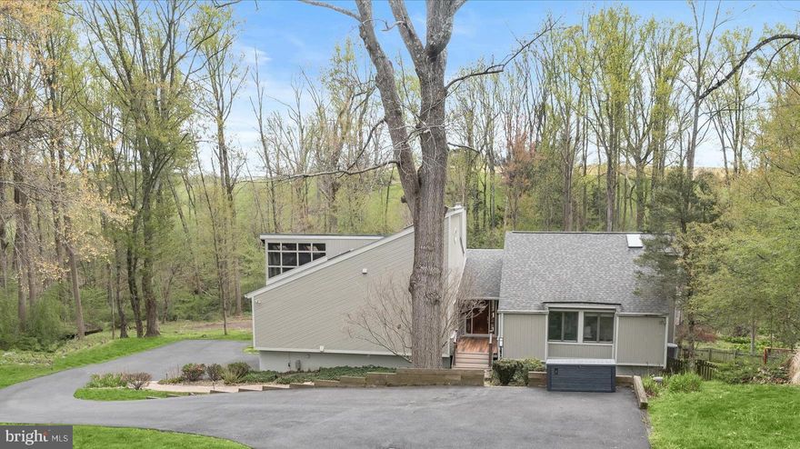 Stunning contemporary home nestled on a quiet cul-de-sac in the sought-after The Heritage community set on a premium 3.3-acre homesite backing to woods and farmland with breathtaking, picturesque views framed by soaring vaulted ceilings and dramatic floor-to-ceiling windows, while the upgraded walkout lower level offers a full bath and potential fourth bedroom. The open-concept living and dining areas showcase refinished hardwood floors, walls of glass, and a striking wood-burning stove set against a custom stacked-stone accent wall. A live-edge wood staircase leads to a loft, ideal for a home office or creative retreat.  The custom-designed gourmet kitchen features rich wood cabinetry, stainless steel appliances, an upgraded induction cooktop, an oversized island breakfast bar, and a stunning herringbone tile backsplash. The adjoining breakfast room opens to the screened porch surrounded by floor-to-ceiling windows and panoramic skyline views.  The primary suite is a true sanctuary, highlighted by updated French doors, exquisite inlaid hardwood flooring, a walk-in closet, and frosted French doors leading to a luxurious spa-inspired bath. Rich wood cabinetry, designer tilework, a corner soaking tub, an oversized frameless shower, heated tile floors, and a heated towel rack continue the home’s elevated design. Two additional hardwood-floor bedrooms and a beautifully appointed hall bath complete the main level. A stacked-stone staircase leads to the refinished lower level.  The finished lower level features a generous living area with direct access to the patio and backyard, a full bath, a versatile bonus room or potential fourth bedroom, and a mudroom with convenient entry to the garage. Outdoor living feels like a private retreat with a partially fenced yard, hot tub, dedicated fire pit area, surrounding bike trails, a nearby stream, and unforgettable views in every direction.  An oversized finished 2.5-car garage includes an exercise area with mounted TV, finished flooring, drywall, lighting, and built-in storage.  Additional highlights and recent upgrades include a surround sound speaker system, radon mitigation system, 2021 roof, two new hot water heaters (2021), new well pump (2021), 2025 pH water balancer, and 2025 hot tub updates including new control panel, salt system, and cover.