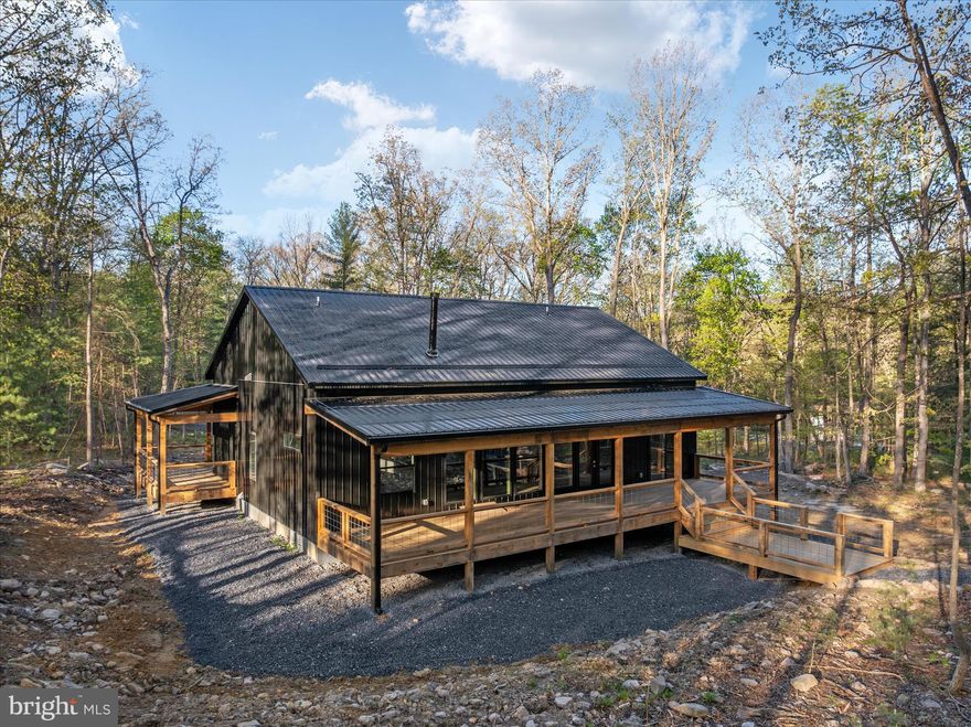 There’s a certain kind of quiet magic in the mountains of West Virginia—where the air feels a little softer, the stars shine a little brighter, and life settles into a slower, more meaningful rhythm. This brand-new, barndominium-inspired cabin was thoughtfully created to meet that moment, blending modern design with the timeless pull of nature. Set against the backdrop of the George Washington National Forest, this striking 1776 sq ft retreat offers a seamless connection to the outdoors, where your backyard stretches into protected wilderness. The bold black metal roof and siding create a clean, architectural presence among the trees—low-maintenance, yet undeniably refined. Inside, the home unfolds with ease. One-level living invites comfort and simplicity, with three bedrooms and two full baths designed for both everyday living and effortless hosting. The spaces feel open yet grounded, perfect for gathering with family or slipping away for a quiet weekend. In the kitchen, concrete countertops and a matching backsplash—soon to be completed—will bring a modern, organic finish that complements the home’s natural surroundings. Ceramic tile in the bathrooms and mudroom adds durability with a polished touch, while carefully chosen lighting in the dining area sets the tone for long, unhurried meals. Evenings are meant to be savored here. A newly built fire pit waits for stories, laughter, and stargazing, while the peaceful setting offers a sense of retreat that’s increasingly rare. Practical details have been thoughtfully considered: a transfer switch is already in place, with pads ready for a future generator and propane tank, offering flexibility and peace of mind. A hot tub hookup on the back porch invites you to create your own private escape, and an electric vehicle charger out front adds a modern convenience that feels right at home. Tucked just 10 minutes from Wardensville, you’re close to a charming small-town rhythm—local markets, cozy dining, and everyday essentials—yet worlds away from the noise. This is more than a home—it’s a place to gather, to recharge, and to live more intentionally.