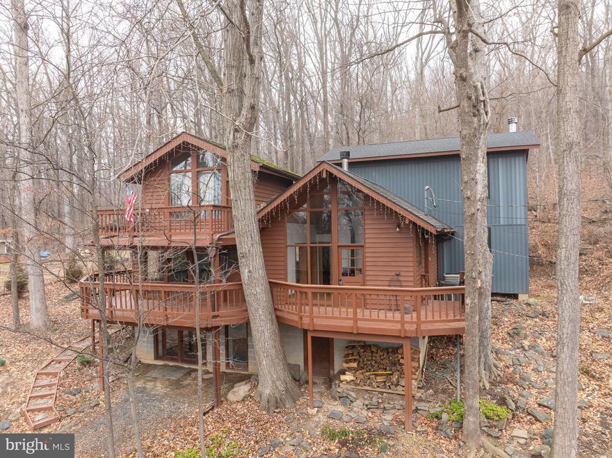 Want a home to get away from it all? This lovely home has so much to offer inside and out. It is surrounded by trees and backs to national forest land and the Appalachian Trail. The multiple decks offer seasonal views and plenty of peace and quiet. Imagine enjoying your favorite beverage at the end of the day while watching the sunset from here. Once inside, you will feel like you are nestled inside a tree house far removed from the hustle and bustle of daily living. The layout is unique and spacious, offering areas for gathering together or withdrawing in solitude. The floor to ceiling windows in the kitchen make it easy to wake up to your morning coffee. The wood stove here will take the chill off the coldest morning. Enjoy your meals in the spacious eat-in area or the separate dining room. The semi-open floor plan keeps you connected to the large living room as well. Your favorite room though, may be the family room with its grand stone fireplace and built-ins. The room that had been used as a library features ladder access to a loft area that makes a great hide-a-way or playroom. The laundry room is also located on this level. Upstairs the primary bedroom takes you even higher with its own deck and a quirky, but totally functional ensuite bathroom. The second bedroom is huge and has its own staircase. The lower level presents many options – game room, art studio, or home office – and the recessed lighting and glass doors keep it light and bright. Another unfinished room on this level is great for storage or hobbies. There is also a lower-level workshop accessible from outside. This home is on public water. See documents for health department records on the septic system. This home also comes with a large shed and plenty of firewood. The many flowering plants around the property are just about to pop. All this quiet serenity is located just minutes from major commuter routes. The almost one-acre property is composed of several lots deeded together; one is across Cub Lane. You can be living here by spring and enjoy all the flora and fauna the best of Almost Heaven West Virginia has to offer.
