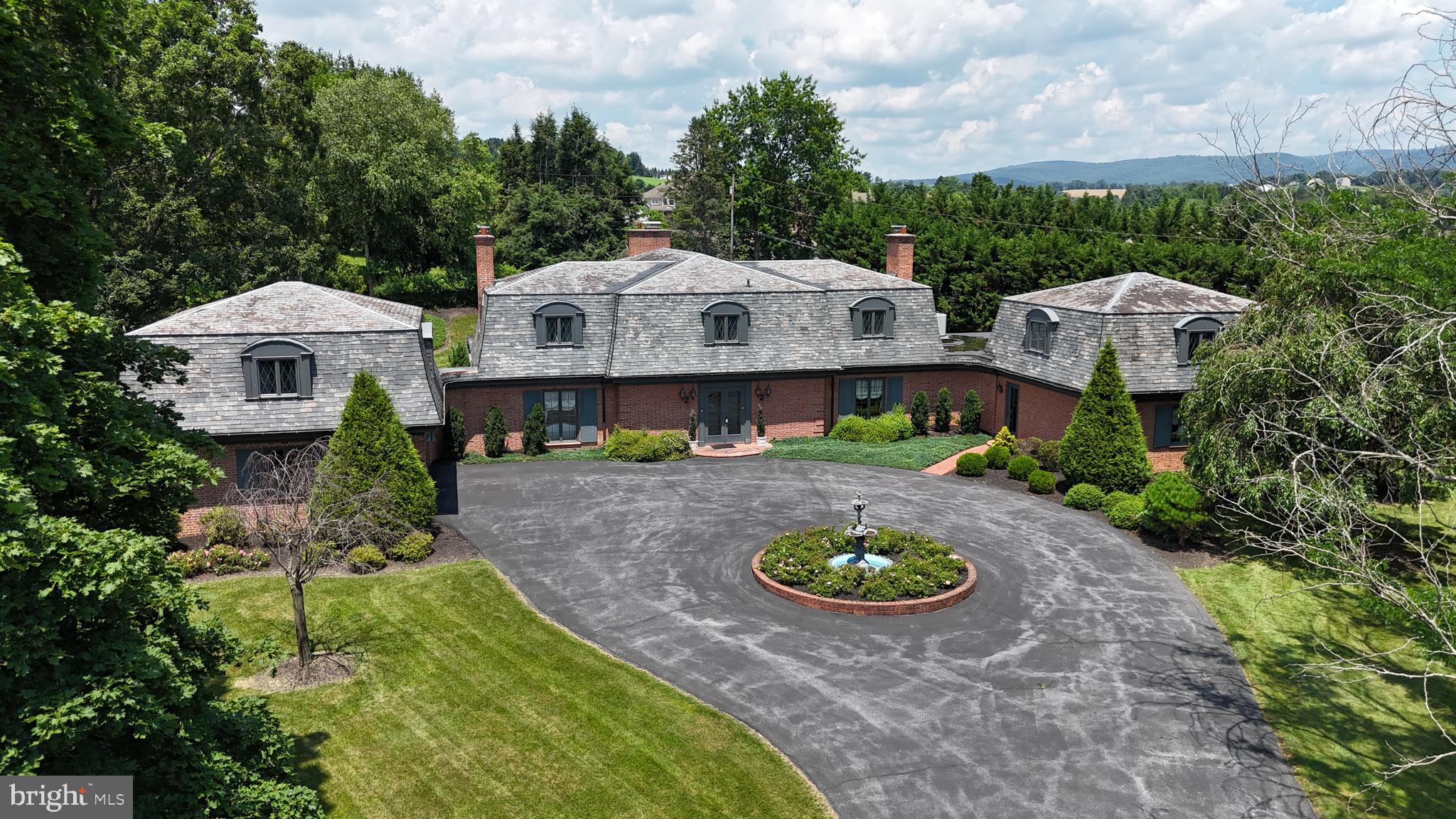 This Dutch colonial home epitomizes elegance and quality. As you approach, the grand brick entryway, circular drive, and fountain set a majestic tone. The main entryway is even more spectacular, featuring an exquisite foyer with a curved stairway, marble floors, and a wet bar, perfect for entertaining. The craftsmanship is evident in the stunning trim work throughout the house. The library boasts a gorgeous fireplace, built-in bookcases, and Parque wood floors, also visible throughout the home. The south sunroom offers floor-to-ceiling windows, marble floors, and 9 ft ceilings, and the north sunroom mirrors these features and provides exterior access to the rear yard. The impressive living room transports you to a European mansion with its large fireplace, exotic trim with gold flake paint, and wood floors. The formal dining room is spacious yet warm, featuring a wood fireplace and a stunning chandelier. The kitchen has a unique feel with exposed brick walls and floors, a large center island and breakfast bar, a built-in cooking alcove with a range and double oven, ample counter and cabinet space, and a wine rack near the walk-in pantry. The east wing of the home includes a more casual entryway, a laundry/mud room, and a sitting room that could serve as a main-level bedroom with an accessible full bath. Stairs from the laundry room lead to a versatile den with a built-in wet bar, ideal for an office, studio, or game room. The upper-level living space is equally impressive, featuring a large hallway with cedar-lined closets and three additional bedrooms. The primary suite includes an ensuite bath with a walk-in tile shower, a separate soaking tub, and a sauna. The large bedroom has five cedar-lined closets. Two more generous bedrooms share a true Jack and Jill bath with a shared tub/shower and separate vanity sinks. The large garage on the southwest side of the home offers ample storage with a full 24x22 storage area above. The nearly 2 acres of ground are perfectly manicured, creating a park-like setting with stunning mountain views. Please Do Not enter the premises without an appointment or permission.