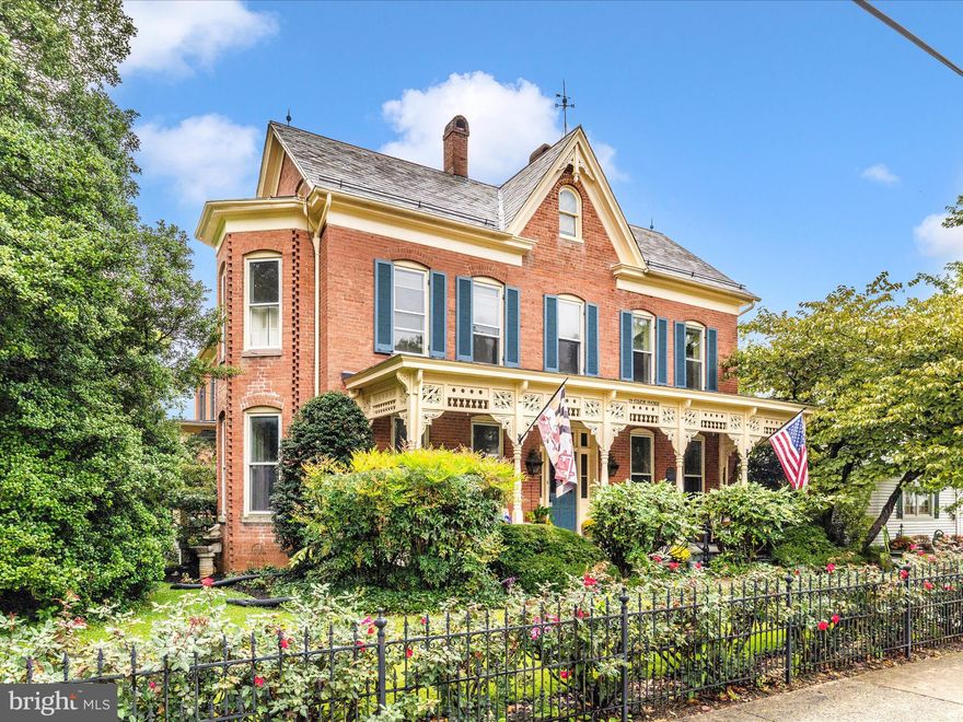 Discover timeless character and a rare offering in Walkersville at 29 Fulton Avenue. Built in 1900, this stately three-story brick Victorian has been lovingly restored over time, blending preserved architectural details with thoughtful modern updates for today’s lifestyle. The exterior walls, 3 bricks thick and crafted by Walkersville Brick & Tile Works stand as a testament to the lasting craftsmanship. Inside, more than 3,000 sq feet of finished living space is enhanced by soaring 10’+ ceilings, tall proportioned moldings, decorative crown details, heart pine hardwood floors, transom windows, and intricate ceiling medallions. Built-in display cabinetry, pocket doors, and even a decorative newel post cap that conceals a secret compartment remain beautifully intact. The grandeur of this home reveals itself the moment you enter, where original character immediately transports you to an era bygone. The dining room, perfect for large gatherings, features bay windows with plantation shutters, a wood-burning fireplace with an elaborate mantel, a tray ceiling with a ceiling medallion, and a statement chandelier. A true centerpiece of the home, the modernized kitchen boasts ten-foot pocket doors, a masonry wood-burning heater crafted from original bricks, soapstone counters, stainless steel appliances, and abundant maple cabinetry. The recent remodel provides beauty and functionality, offering plenty of space for cooking and entertaining.  Access to the second staircase is shared between the kitchen and the family room. A bonus room off the kitchen has a 2nd wall oven and has been used as a butler's pantry room by the current owners. The family room centerpiece is the Barlett Hayward Latrobe stove, manufactured in Baltimore, Md, and modified for propane which adds warmth and a historical feel to the room. Other features are the surround sound access grates, secret storage areas, (2) ceiling medallions with ornate chandeliers, the second full bath with stained glass doors, and a claw-foot bathtub. The third staircase can be found in this room and is adorned with a custom iron handrail. A mud room with heated floors and floor-to-ceiling cabinetry serves as a second entry point to the home and flows into the family room. Cozy up with a book and watch the snow fall from the four-season room with floor-to-ceiling Eze-Breeze windows and a propane stove. Four bedrooms, a modern full bath, and laundry are all generously sized and full of natural light. The primary bedroom has a bay window with plantation shutters and direct access to the full bath. A rear bedroom has access to the third staircase, believed to be used by the house staff in the late 19th century. A walk-up attic with over 1,700 square feet of floored, fully insulated space provides endless possibilities for additional finished rooms. Outdoor living is equally inviting. A cozy side porch and a large covered front porch with intricate gingerbread trim provide the perfect backdrop for quiet mornings and unhurried evenings. A custom wrought iron border fence and handrail complements the home’s Victorian style, and is lined with fragrant red roses, creating a striking first impression. Gas lit front porch lamps frame the front entry and greet you with a warm, flickering light, while details like the original mail slot and intricate mechanical doorbell preserve the home’s historic charm. The roof is a combination of slate and asphalt and is equipped with half-round gutters and period lightning rods, while the large driveway leads to a darling carriage house adding function and character.  Located in the heart of Walkersville, this home offers a lifestyle that blends community, convenience and charm. Walk to schools, the library, church, and restaurants. Opportunities like this are rare, and it's ready for its next chapter! This isn’t just a place to live, but a place to grow, create lasting memories, and carry forward with pride. Watch the YouTube tour!