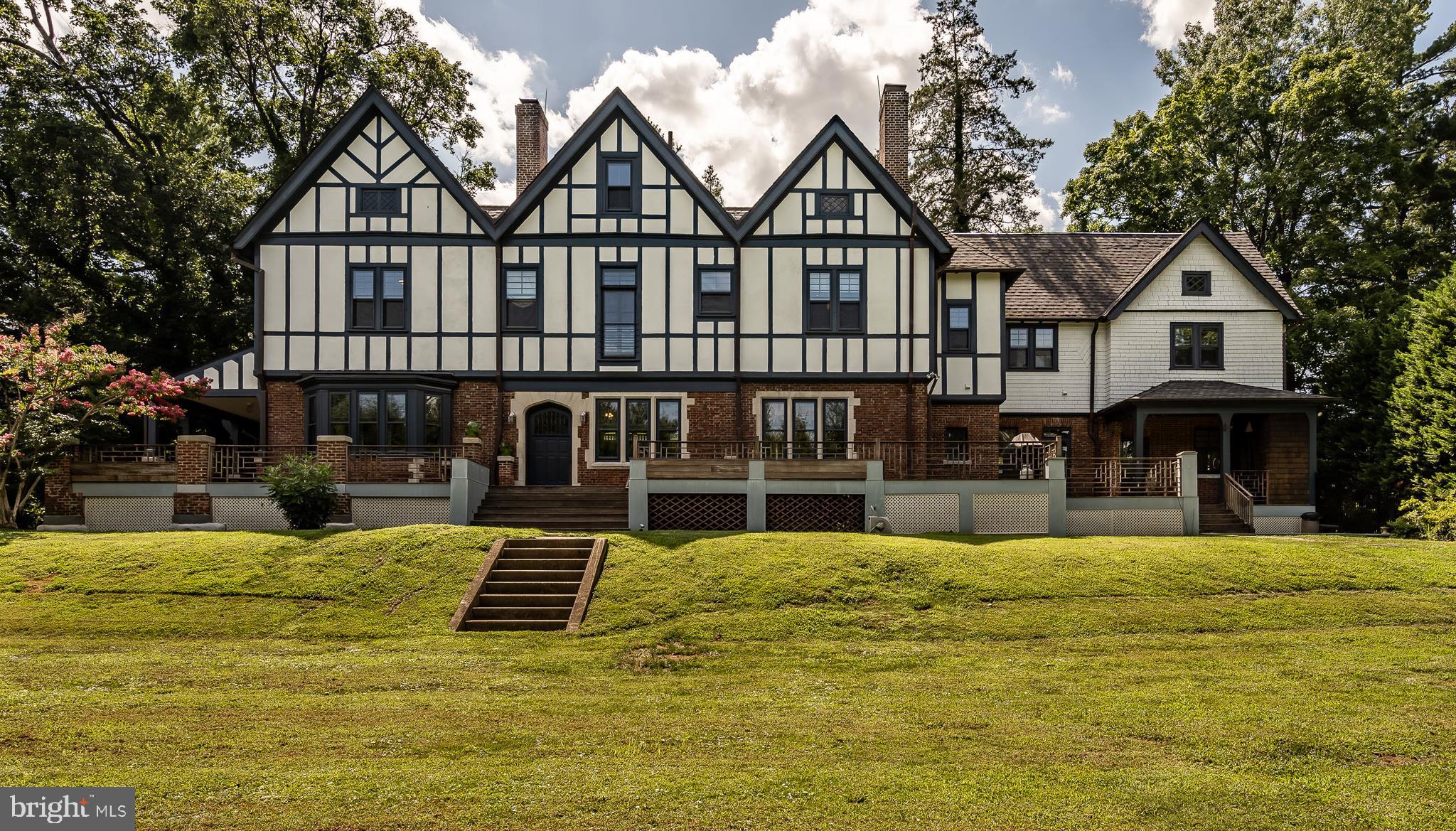 The best of both worlds! Beautifully restored English Tudor that has been updated for modern living while lovingly maintaining the character of the period. Red Bud Manor was given as a wedding gift to a member of the prominent Ashbridge family in 1899 and is said to be inspired by the Shakespeare Globe Theatre in Stratford-upon-Avon. A major renovation created a large gourmet kitchen area that features a radiant heated graphic cement tile floor, glass front storage, top of the line appliances and expansive eat-in kitchen area. The kitchen is anchored by a large marble island with a commercial Blue Star range, a separate prep area, as well as a massive reconfigured pantry area for storage. Other parts of the renovation included multiple bathrooms and a second-floor in-law/au pair suite with full kitchen. Two-200 Amp service panels were installed along with five-zoned forced air heating and air conditioning. The main level has 10+ foot ceilings, original quarter sawn oak paneling and millwork and an open flow to allow for large gatherings. The living room and dining areas can be closed off to provide privacy when desired. Each room features a fireplace as well as rich hardwood flooring. Upstairs, there are six bedrooms with original yellow pine flooring, and includes a live-in suite with a gourmet chef's kitchen and renovated bathroom. Walk out to a 4000 square foot deck that wraps around the length of the back of the house. Railings inspired by one of the custom designed exterior doors, built-in seating, and decking are constructed from Brazilian Ipe, a gold standard among decking materials. The deck overlooks a huge, tiered backyard that has raised planting beds, a potting shed, and perimeter plantings. Coupling that with the exquisite Flemish bond brick pattern of the home and copper gutters, it feels very much like the English countryside. A large unfinished basement with brick arches can accommodate a future wine cellar, and the enormous walk up open floor attic can be converted into another 1500 square feet of customized living space. A wealth of future possibilities exist. The home is well situated on the Main Line, within walking distance of the Rosemont Septa, Ashbridge Memorial Park and all that Bryn Mawr shopping and dining has to offer. This is truly a one of a kind estate home.