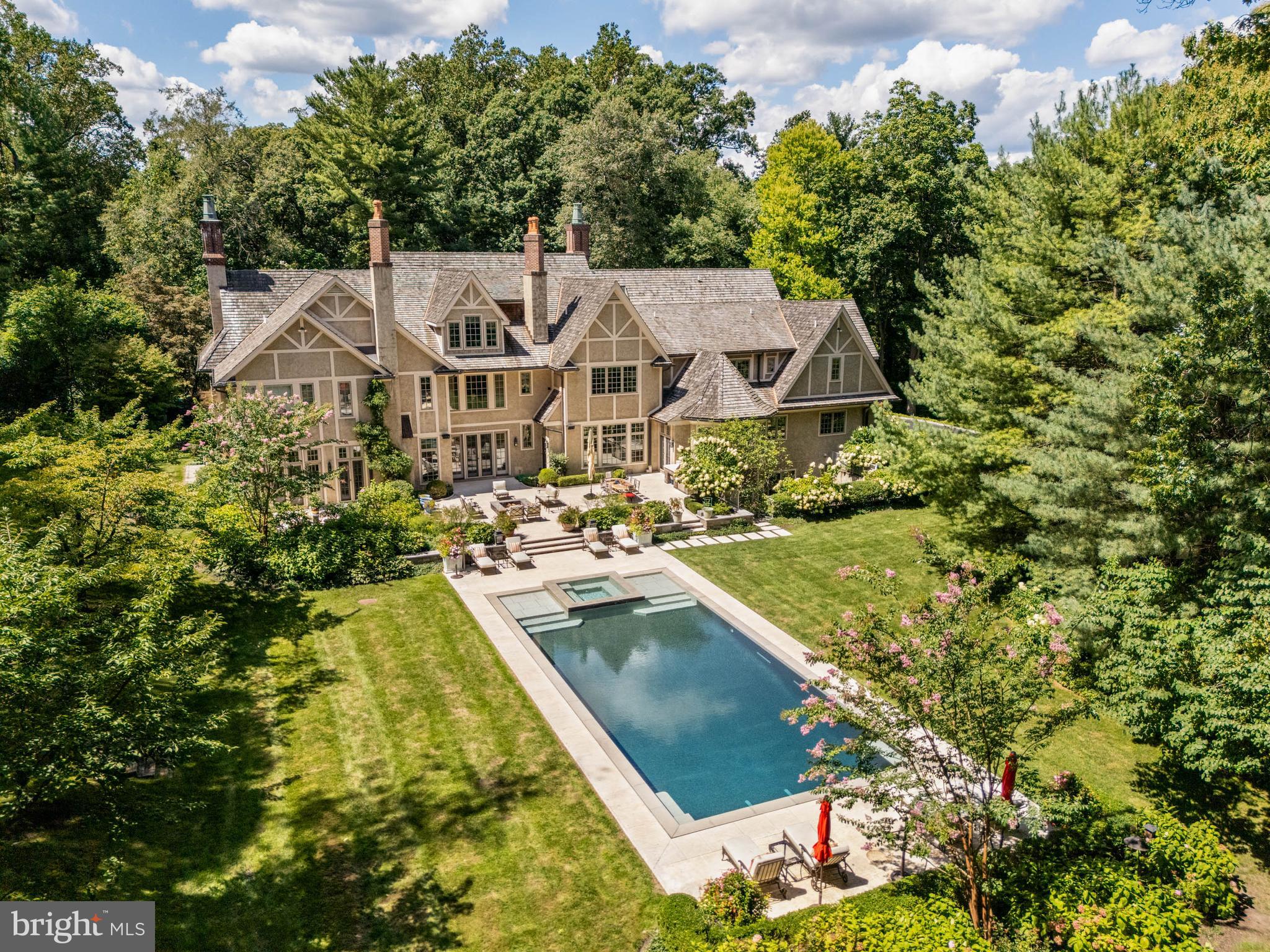 Surrounded by a perimeter of mature forest including evergreens and accessed through a formal gate, Arbor Aves is a Stone Manor estate positioned on one of Northside Haverford’s most coveted and quiet lanes. The front façade combines extraordinary stone and brickwork in a composition of enduring elegance, while the rear elevation, accented with board and batten details, is breathtaking in its symmetry and scale. Framed by gardens and hardscaping designed by Chuck Hess, the light-stone terraces, resort-quality vanishing-edge pool with perimeter overflow, spa, fire-pit, and a fully equipped outdoor kitchen with stainless steel grill create a setting where everyday living feels like a retreat.
A front-to-rear center hall with inlaid stone floors, and a sitting nook sets a tone of refinement the moment you enter. The living room combines architectural balance with warmth, featuring a fireplace, abundant natural light from 2 exposures, and a charming front window nook that invites reading, conversation, or quiet reflection. The dining room is enriched with ceiling moldings, a cushioned window seat, and ornamental fireplace, while the library offers finely crafted millwork and the solarium glows with wrap-around windows and honed slate flooring. Throughout the main living areas, hardwood floors of white oak—aligned with today’s design preferences—underscore the home’s sophisticated yet timeless palette. Five fireplaces are placed across the home’s 4 finished levels, blending architectural beauty with comfort.
At the heart of the residence, the Clive Christian kitchen is a showpiece of honey-toned cabinetry, polished Calacatta Gold marble, and professional La Cornue range, anchored by an island with seating for 4. The adjoining breakfast room, crowned by a soaring 12-foot ceiling, overlooks the gardens and flows to the family room, where a fireplace and custom shelving invite gathering. Thoughtful design touches abound: a walk-in pantry with Thermadore wine storage and direct inside access to the garage simplifies unloading groceries, while a “command center” with built-in desk, cabinetry, and shelving provides a practical hub for household management. Crestron automation makes listening to music or controlling lighting and HVAC a breeze.
The primary suite is a retreat of extraordinary scale and comfort, complete with a private sitting room and fireplace, a beverage center, dishwasher, 2 fully customized walk-in closets, and dual spa-like onyx baths with soaking tub, slab counters, and shared double-sided shower. A 2nd-floor landing introduces another architectural moment—a cozy sitting nook with custom shelving and a window overlooking the front courtyard, creating a quiet retreat above the main foyer. Five additional en-suite bedrooms complete the family level, while the 3rd floor provides flexible space or an in-law suite with living room, generous bedroom suite with full bath, walk in closet, cedar closet, and additional storage.
The finished lower level is designed for recreation and entertaining, with a professional gym, state-of-the-art theater, walk-in wine cellar, and full wet bar with large island for entertaining, full size dishwasher, refrigeration and cabinetry. Two full bathrooms serve this level: one positioned as a dedicated poolside cabana with changing area and direct access to the gardens, the other adjacent to the exercise room. Every space has been crafted with the same level of finish found throughout the home. An elevator serves all 4 levels.
Green features—cedar shake roof, Pella Architectural Series windows, blown-in insulation, Energy Star HVAC, permeable pavers, and water-saving fixtures—demonstrate the home’s thoughtful design and efficiency.
Arbor Aves is more than a residence; it is an experience. Morning light fills the whole rear expanse, spend mornings or afternoons around the infinity pool or in the theater, and evenings draw family, friends to the terraces,