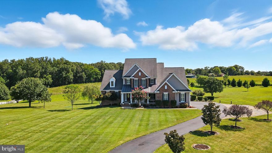 Welcome to Bloomsbury Farm Estates, where timeless design meets modern comfort. This 5-bedroom, 6.5-bath estate offers over 6,530 finished square feet on 5.72 private acres, complete with a 3-car garage, TWO Primary Suites, finished walkout basement, and heated saltwater pool surrounded by views of rolling hills with NO HOA! The magnolia-lined asphalt driveway leads to the home’s inviting covered front porch. Step inside the foyer and you’ll find wide-plank hardwood flooring, extensive oversized trim, and custom plantation shutters throughout, setting the tone for the home’s craftsmanship. French doors open to the bright living room with a coffered ceiling, columns, and a gas fireplace with custom built-ins, overlooking the gourmet kitchen. The formal dining room (currently used as a home office) is designed for effortless entertaining, opening directly to a butler’s pantry complete with custom cabinetry and sink—a seamless connection between kitchen and dining spaces that adds both function and elegance. The heart of the home is the gourmet kitchen, anchored by a striking wood coffered ceiling that adds warmth, depth, and architectural character. The kitchen is outfitted with stainless appliances including GE dual ovens, a gas range, a Samsung refrigerator, dishwasher, dual pantries, and a large center island with seating. Just off the kitchen, the family room offers a cozy retreat with plush carpeting, custom built-ins, and a gas fireplace, creating a warm and inviting space for everyday living. The home extends outdoors with a screened porch featuring Trex flooring and a ceiling fan, overlooking the sparkling pool. Accessible directly from the living room, it’s the perfect spot to relax and take in views of the property. For added convenience, a half bath is situated in the main hallway for visiting guests. The main-level laundry room is both stylish and functional, featuring a deep utility sink, custom wood cabinetry with soft-close doors, and a convenient drying rack. Designed with organization in mind, this space makes everyday tasks easier while maintaining the home’s elegant design aesthetic. This home offers the rare luxury of two primary suites, one on the main level for convenient first floor living and another on the second level. The main-level primary suite is a retreat of its own, with a tray ceiling, walk-in closet with custom built-ins, and spa-like bath featuring dual vanities, a soaking tub framed by an etched glass window, water closet, and a tiled walk-in shower. Upstairs, the second-level primary suite showcases tray ceilings, a ceiling fan, and plush carpeting, along with a walk-in closet with custom built-ins. The spacious bath includes tile flooring, dual vanities, a soaking tub set beneath a large window, a private water closet, and a second walk-in closet with built-in shelving and automatic lighting—combining elegance with everyday functionality. Completing the second level are three bedrooms each with their own en-suite bath and closet. The spacious finished basement provides an additional level of living and entertaining space. A well-appointed kitchenette makes hosting gatherings effortless, while the expansive recreation room with oversized windows and walkout access to the patio and pool is ideal for movie nights, game tables, or casual entertaining. A dedicated gym—easily convertible into a sixth bedroom with a large walk-in closet—offers flexibility for fitness or guests, and a full bath with tile finishes ensures comfort and convenience. In addition to its expansive finished spaces, the basement also includes an unfinished area ideal for storage, keeping seasonal items, recreational gear, or household essentials neatly tucked away without sacrificing living space. Outdoors, enjoy the heated 6-foot-deep saltwater pool, enhanced by vinyl fencing, a paver patio, and stamped concrete surround—an entertainer’s dream and a true extension of the home’s living space.