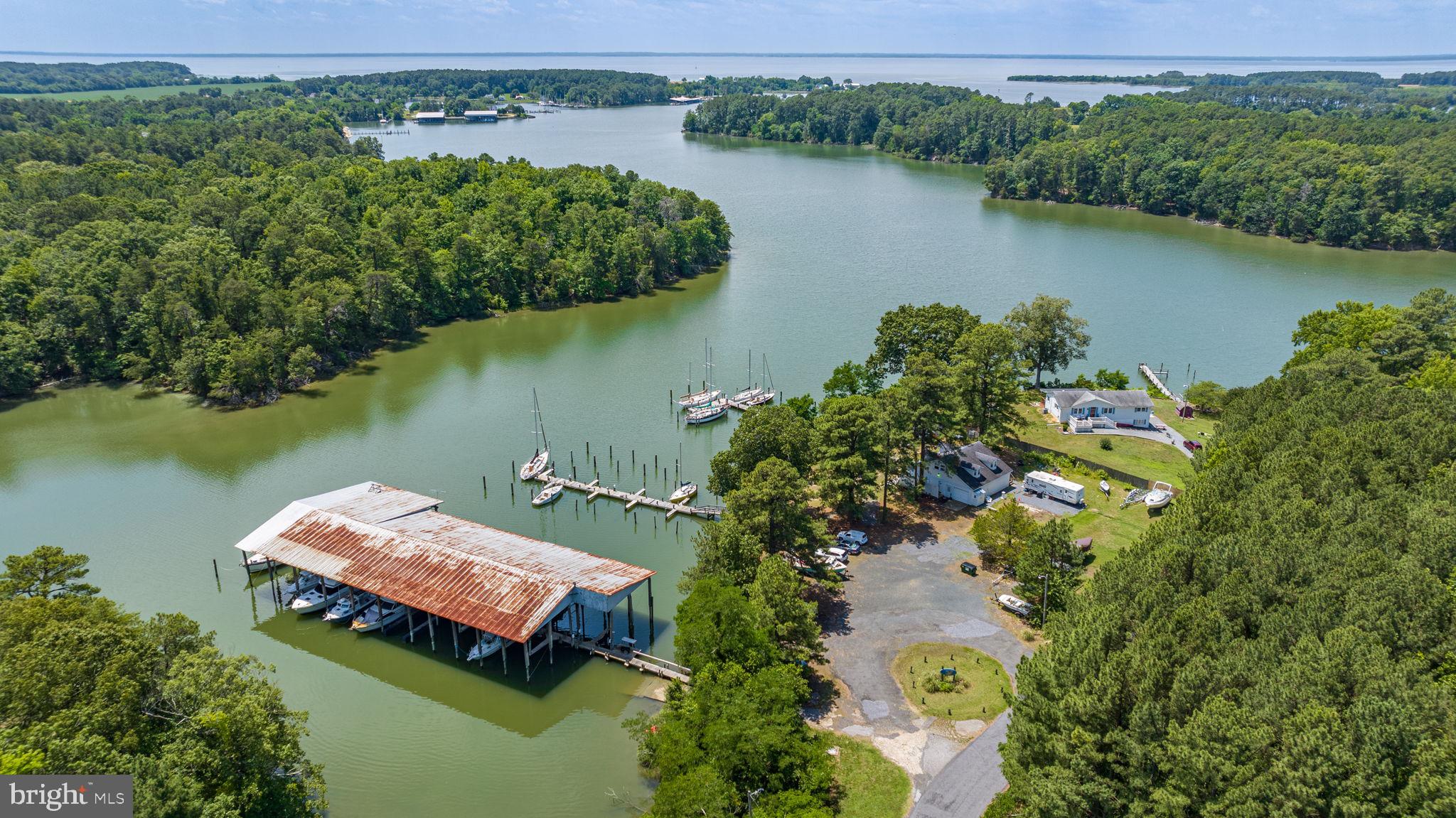 Price reduction of $25,000! Waterfront on Jutland Creek off the Potomac River. Serene one-acre property current operated as a small commercial marina with deep water piers in a protected cove. Awesome views. This property has potential in several directions. Since the 1970s, the property has been continuously operated as a marina, currently BluHaven Piers, originally Misty Cove Marina. Be an owner-operator and live in the main marina building on the property. Or renovate/convert the main building into a primary or secondary residence and apply to rezone the property as residential, which may be a more valuable long-term option.
Property includes a main building serving as the marina reception, with an upstairs office, a garage, and showers and bathrooms for marina slip holders. There are several small out-buildings for storage or a workshop. There are about 50 boat slips on three piers, one of which is covered. Approximately 7 feet water depth at the end of the piers. Electricity and water provided to many of the boat slips. This beautiful property is in search of a caring owner with vision and is priced accordingly.
The absentee owner has retired and put the marina into a self-service mode, awaiting a new owner. No marketing has been done since before the pandemic. Since the summer of 2023, several improvements have been made, including removing a few abandoned boats from the yard and repairing one of the small storage buildings. As an ongoing business, the marina breaks even on an operational basis before any personnel costs. Slip fees currently cover insurance, property taxes, electricity, waste removal, telephone, web site, and minor maintenance. Property is sold strictly “as is”.