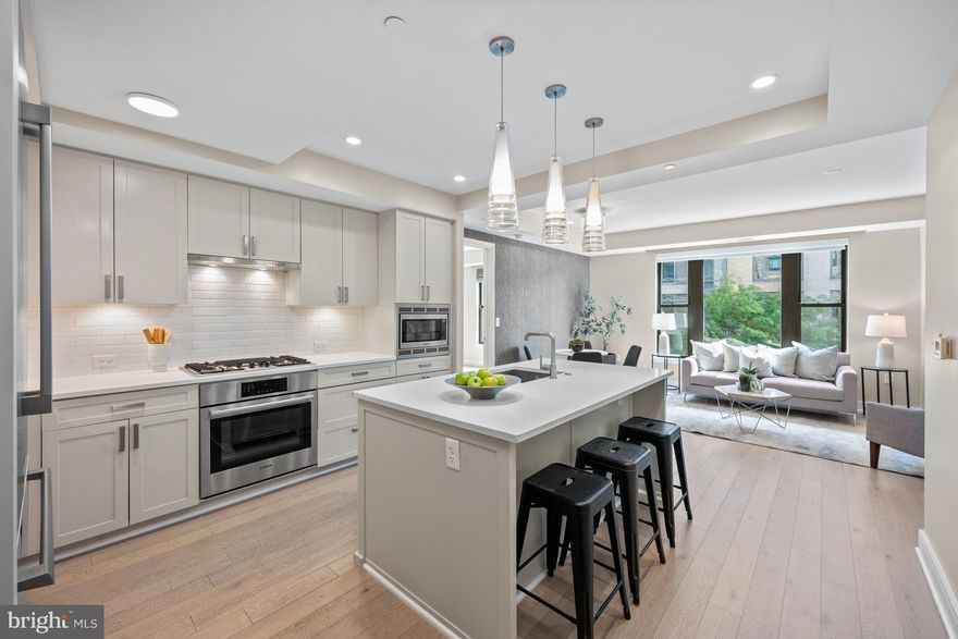 Introducing The Stonehall Condominium, a luxury boutique residence ideally situated in the heart of downtown Bethesda, Maryland. This beautiful two-bedroom, two-bathroom home offers nearly 1,000 square feet of thoughtfully designed living space, enhanced by contemporary designer finishes. Upon entry, you are welcomed into an open-concept floorplan that seamlessly blends style and functionality. The kitchen is a true centerpiece, featuring sleek quartz countertops, premium Bosch stainless steel appliances, and a Thermador refrigerator. An oversized island provides ample prep space and casual bar seating, framed by modern pendant lighting. Wide-plank hardwood floors in a soft, neutral palette create a warm and inviting backdrop. Expansive windows flood the interior with natural light, highlighting a dedicated dining area accented by a fabulous light fixture and elegant wallpaper detail. The living area serves as a comfortable gathering space—perfect for relaxing or entertaining.
The primary suite has been thoughtfully enhanced with custom closet cabinetry and a spa-inspired en-suite bath, complete with dual vanities, backlit mirrors, and a spacious walk-in shower. The secondary bedroom is equally inviting, offering its own walk-in closet and convenient access to a well appointed hall bath featuring a shower-tub combination. Versatile in design, this space also lends itself perfectly to a private home office. A stackable washer and dryer are discreetly tucked into a hall closet.
A true highlight of this residence is the separately deeded parking space, which conveys with the unit—an exceptional convenience in downtown Bethesda. For added flexibility, a second parking space is also available for purchase. Residents of The Stonehall Condominium enjoy an impressive suite of amenities, including two rooftop terraces, a community garden, and sweeping views of Bethesda. A stylish resident clubhouse offers an inviting space for gatherings or quiet relaxation, while the fully equipped fitness center is easily accessible on the second floor. Ideally situated in a peaceful pocket of downtown, the location offers the best of Bethesda just outside your door—renowned dining, boutique shopping, and vibrant entertainment. With both the Bethesda Metro and Medical Center Metro just moments away, commuting is effortless. With its thoughtful layout, premium finishes, and unbeatable location, this residence presents a truly exceptional opportunity.