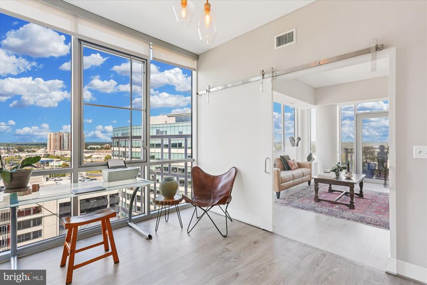 Available 12/1/2025.
One-of-a-Kind Redesigned Corner Unit 2BR 2BA + DEN in Pike & Rose!
Experience luxury living in the heart of Pike & Rose with this rarely available two-bedroom, two-bath plus den condo — the only residence in the building boasting a custom, redesigned layout! Thoughtfully reconfigured to maximize light and flow, this residence seamlessly connects the primary suite with two entrances, den, and living areas in a bright, open, and entirely wheelchair-accessible configuration that feels both expansive and welcoming. Enjoy sweeping east and north-facing views from the 14th floor, where stunning sunrises and the dynamic energy of the city unfold just outside your windows.  Walls of floor-to-ceiling glass frame the open-concept living and dining areas, anchored by a chef’s kitchen featuring extra-wide prep space between cabinets/cooktop and the waterfall-edge quartz center island, stainless steel appliances, pendant lighting, a breakfast bar, and abundant storage. A charming bistro nook by the window—exclusive to this floor plan—offers a perfect flex space for a reading corner, breakfast area, or compact workspace. Step out onto your private balcony to unwind and take in panoramic views over lush green rooftops and the bustle of Pike & Rose.The versatile den opens to the living room with stylish barn doors and connects to the primary suite via a second set of double doors. Whether used as a home office, media lounge, or guest space, the den can be opened to enhance natural light or closed for privacy.The primary suite is a true retreat, featuring a large walk-in closet and a spa-inspired bath with a double vanity, lighted mirrors, a walk-in shower, and sleek finishes. A clever redesign provides two access points, creating smooth circular flow throughout the unit. A spacious second bedroom and full bath complete this functional floorplan.
Additional highlights include luxury LVP flooring throughout, a tray ceiling with custom lighting in the living room, and a full laundry closet with front-loading washer and dryer. One garage parking space and a private storage unit are also included.930 Rose is a full-service luxury building offering a concierge, secure garage parking, and private elevators. Residents enjoy access to an exceptional rooftop level with a state-of-the-art fitness center, billiards lounge, party room, pet area, and a sprawling outdoor terrace with grilling stations and sweeping 360-degree views.
Located in the vibrant heart of North Bethesda, Pike & Rose delivers unmatched urban convenience. Enjoy walkable access to top-tier dining, shopping, and entertainment—from croissants at Sunday Morning Bakehouse to movies at iPic, bowling at Pinstripes, and rooftop cocktails at Canopy by Hilton. Community amenities include beautifully landscaped plazas, a dog park, and year-round events. With the North Bethesda Metro (Red Line), Whole Foods, Giant, and Strathmore Music Center just minutes away, this location is the perfect blend of modern luxury and city lifestyle.