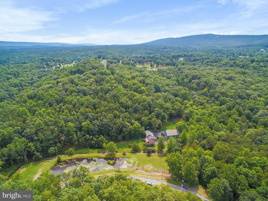 This breathtaking home is awash with possibilities.  Not only a grand estate that any family would be proud to call home, but the makings of a stunning venue, bed & breakfast, vacation rental or second home.  The barn on property is ready for your boutique business, small farm, or hobby.  A portion of grounds could remain lawn or easily convert to parking on site.  Situated on almost 9 acres there are two streams running through the property, one feeds the large pond; you cross it on the quaint stone bridge up the tree shaded drive.  Upon arrival you are greeted with the impressive board and batten sided, 3-level bank barn; the woodwork throughout the home and barn are breathtaking on their own.  The grounds are beautifully kept and the flora flourishes in the well-designed landscaping.  The handsome home has much history, as its construction was started in 1990 and finished in 1991 utilizing material from deconstructed 1740's to 1850's structures and elements.  The most impressive of which are the rustic post and beams, brick fireplaces, wide plank rustic hardwood flooring and strap-hinge interior doors.  The reconstruction honors the history while providing the benefits of modern building practices and daily living conveniences.  The home offers four bedrooms and two and a half baths.  There are two staircases to the upper level with three bedrooms and an office/study.  The property is unrestricted, but the owners have access to Class A Membership at The Woods Resort.  We welcome you to this one of a kind property to see what possibilities it might hold for you.