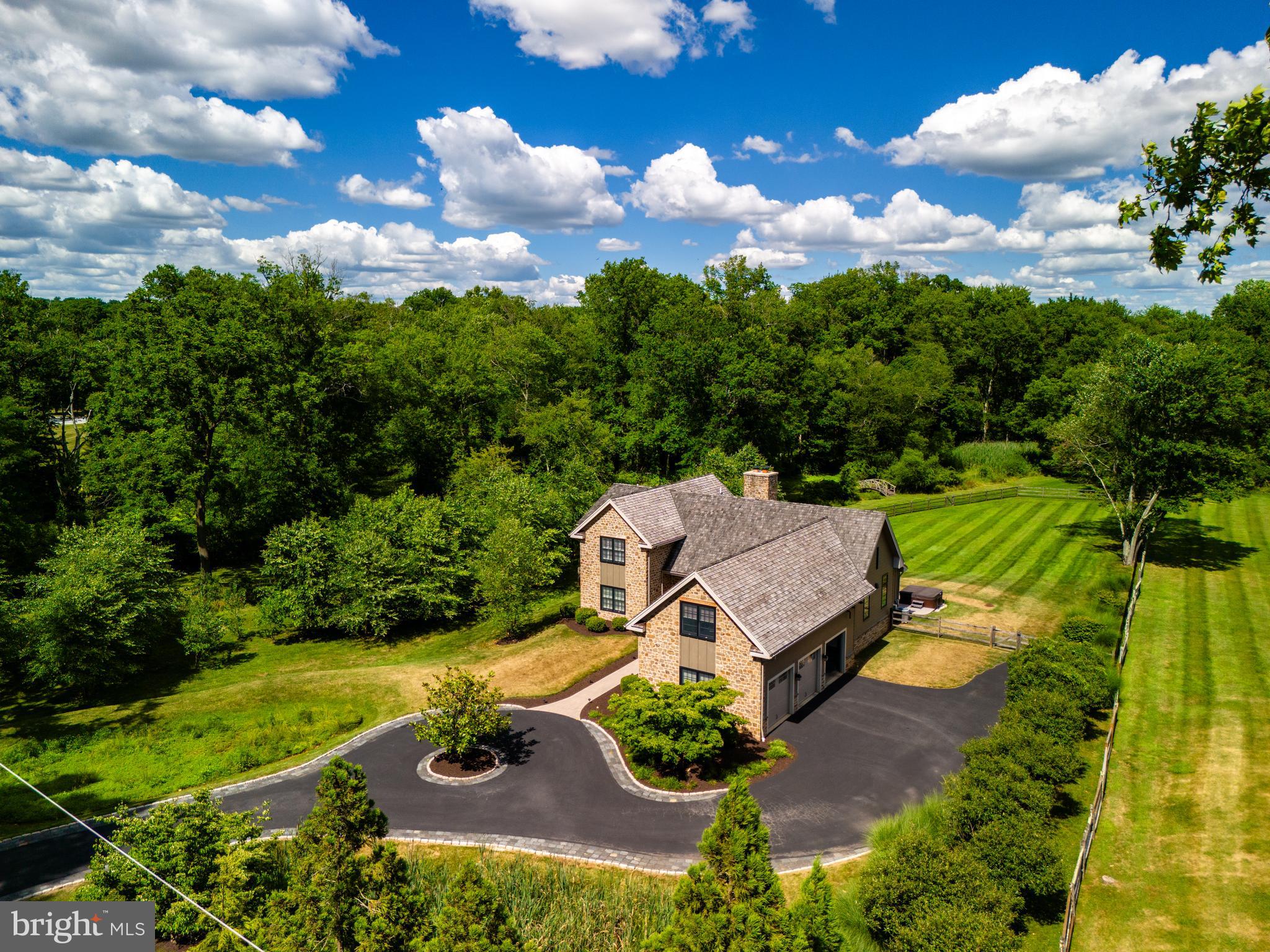 Nestled on 3.3 picturesque acres in Willistown Township, Pennsylvania, this exquisite four-bedroom residence epitomizes the region's commitment to land conservation and harmonious living. Surrounded by sprawling farms and verdant landscapes, this custom-built home is designed to seamlessly integrate with the authentic charm of Chester County.
The exterior showcases hand-split cedar shingles and fieldstone construction, marked by meticulous craftsmanship, including thoughtfully "pinched" mortaring that enhances its rustic appeal. Slat-styled windows illuminate the three-car garage while echoing the classic aesthetics of traditional barns.
Upon entering, one is welcomed into an expansive open-concept space that seamlessly combines the living, dining, and kitchen areas. Boasting soaring ceilings that exceed 25 feet, the interior is anchored by elegant steel turnbuckles that grace the peaked roof. A sophisticated color palette unifies the various spaces, while a gas-burning fireplace serves as a focal point within the seating area. The dining space is beautifully defined by refined lighting, complemented by a well-appointed bar featuring custom cabinetry for wine and stemware, alongside a dedicated wine chiller.
The gourmet kitchen is equipped with top-tier Thermador appliances, a deep stainless-steel prep sink, a striking marble backsplash, and an enormous stone-topped island that invites gatherings. Abundant windows offer captivating views of the surrounding landscape, while a generous laundry and multi-purpose utility room complete the main level, all connected by rich ash-colored hardwood flooring.
Three steps lead to an expansive primary suite that offers a luxurious retreat. The adjoining bathroom features a large, seated shower, an under-window soaking tub, and a double vanity with stone countertops. Continuing the design theme, a rustic barn door opens to a spacious, outfitted closet, leading to the bedroom, which includes a comfortable sitting and work area, with dual windows framing views of the side and rear gardens.
The upper-level houses two generously sized guest bedrooms, accompanied by a shared hall bath adorned with large-format tiles and a seamless glass-enclosed shower. On the kitchen side of the home, an additional staircase leads to a versatile large bedroom, easily adaptable as two separate rooms or a cohesive living and sleeping space, complete with another well-appointed full bath and ample closet space.
The exterior grounds are nothing short of extraordinary, featuring a sprawling lawn enhanced by a large terrace ideal for entertaining. This outdoor oasis includes a grill, a cozy fireplace, and a covered all-season terrace equipped with ceiling fans for warm days and heat lamps for cooler evenings, perfect for enjoying outdoor gatherings throughout the year. A hot tub and fire pit further enrich the outdoor experience, creating a unique, private sanctuary for year-round enjoyment.
Constructed in 2017 with an unwavering attention to detail, this residence reflects the artistry of a professional interior designer, making it a turn-key opportunity for discerning buyers seeking a refined lifestyle in a remarkable setting.