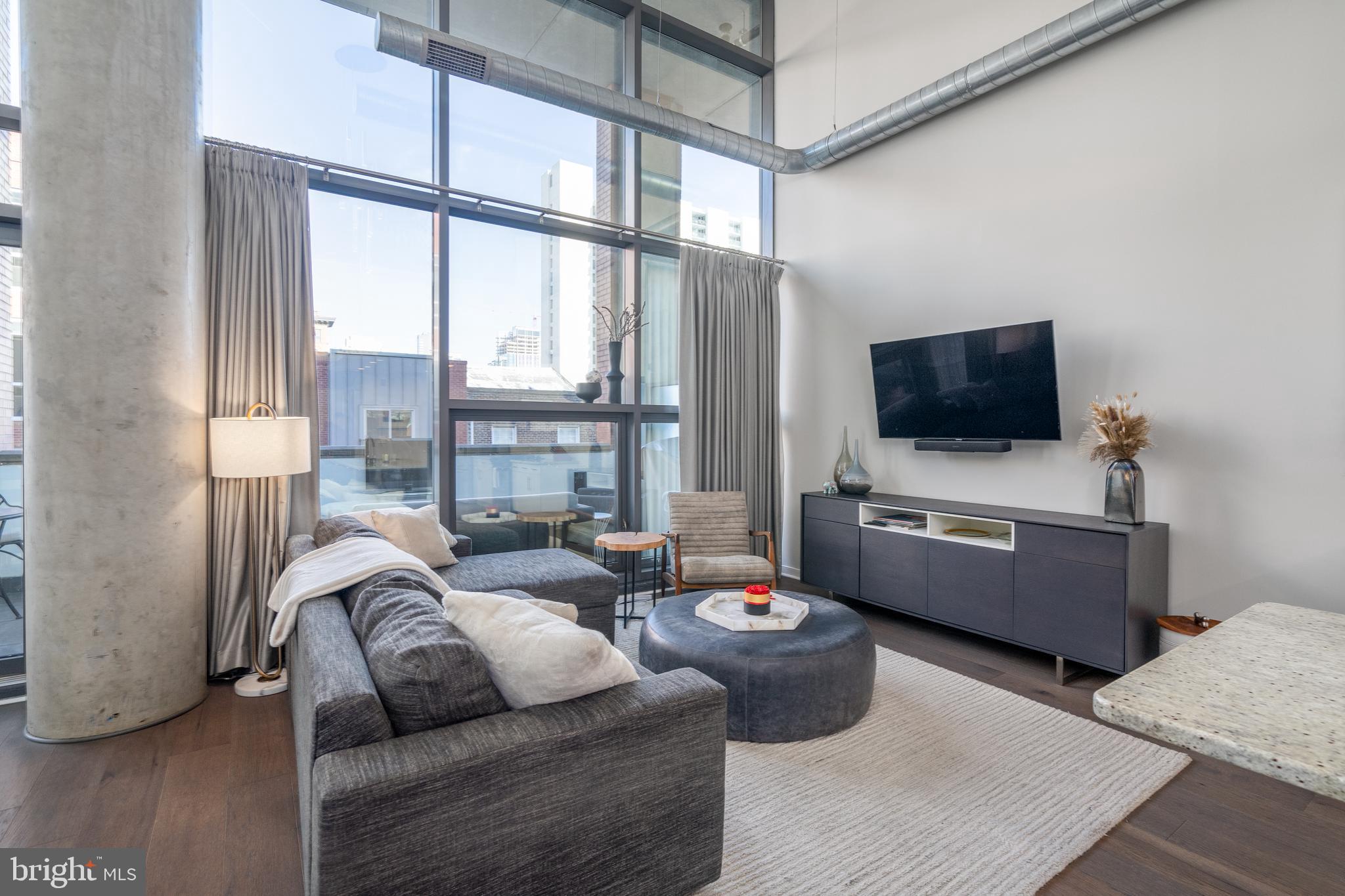 Unit #310 at 1352 Lofts is a bright and airy 2 bed, 2 bath, 1,396 sqft bi-level condo with a private terrace and 1 car garage parking. A large entry foyer with coat closets and built-in storage welcomes you inside. The open main level is filled with natural light from soaring floor-to-ceiling windows that frame the 2-story living room. Industrial-style elements are showcased in the exposed ductwork, iron staircase, and concrete pillars. The sleek kitchen has granite counters, white cabinetry, stainless steel appliances, a tile backsplash, and a unique stainless steel island with seating. Stepping onto the terrace, you'll find a private outdoor space ideal for relaxing with a cup of coffee. Completing the first level is a modern full bathroom off the foyer and a bedroom that could be used as an office and fitness space. Up on the loft level, there's a large primary suite overlooking the living room and the wall of windows. Room darkening drapes allow for privacy when preferred. Concrete floors extend into the walk-in closet that conveniently holds the laundry. There's also a full bathroom. Additional property highlights include a helpful concierge desk and a fantastic location just off Broad St that earns a Walk Score of 99. Schedule your showing today!