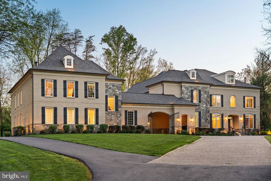 Gracefully positioned at the end of a private cul-de-sac on 2.12 manicured acres, this exceptional French Country estate with a private guest house and resort-style pool offers timeless elegance along the coveted Great Falls–McLean border within the Langley High School pyramid. Built by Keswick Homes, the residence spans 13,448 square feet and showcases soaring ceilings, Brazilian cherry hardwood floors, exquisite millwork, expansive windows, and a three-level elevator. A long private drive leads to a motor court and porte-cochère, setting the tone for the home’s impressive scale and craftsmanship. The chef’s kitchen is beautifully appointed with Sub-Zero, Wolf, and Miele appliances, dual islands, custom cabinetry, and seamless flow to the breakfast room and grand great room with a fireplace. Formal living and dining rooms and light-filled gathering spaces create the perfect balance of luxury and livability. The upper-level primary suite offers a private sitting room, fireplace, balcony, dual custom walk-in closets, and a spa-inspired bath. Rounding out the five en suite bedrooms on this level are a primary-size suite and an independent wing of three generously proportioned bedrooms, one with a zero-entry shower with bench seating, extra-wide doorways, and wide hallway access to the elevator, ideal for multigenerational living. The expansive lower level features a media room, wet bar, billiards, recreation spaces, flex rooms, and guest accommodations. Outdoor living is truly spectacular with a 20x40 heated saltwater pool, retractable cover, outdoor kitchen with Viking appliances, stone fireplace pavilion, and over 6,000 square feet of Pennsylvania bluestone patios and covered porches. A detached 3,000+ square-foot carriage house includes its own kitchen, family room, two bedrooms, and a commercial-grade gym, creating an ideal guest residence, wellness retreat, or multigenerational living environment. Moments from Tysons, McLean, and Washington, this extraordinary estate offers privacy, scale, and resort-style luxury in one of the region’s most prestigious settings.