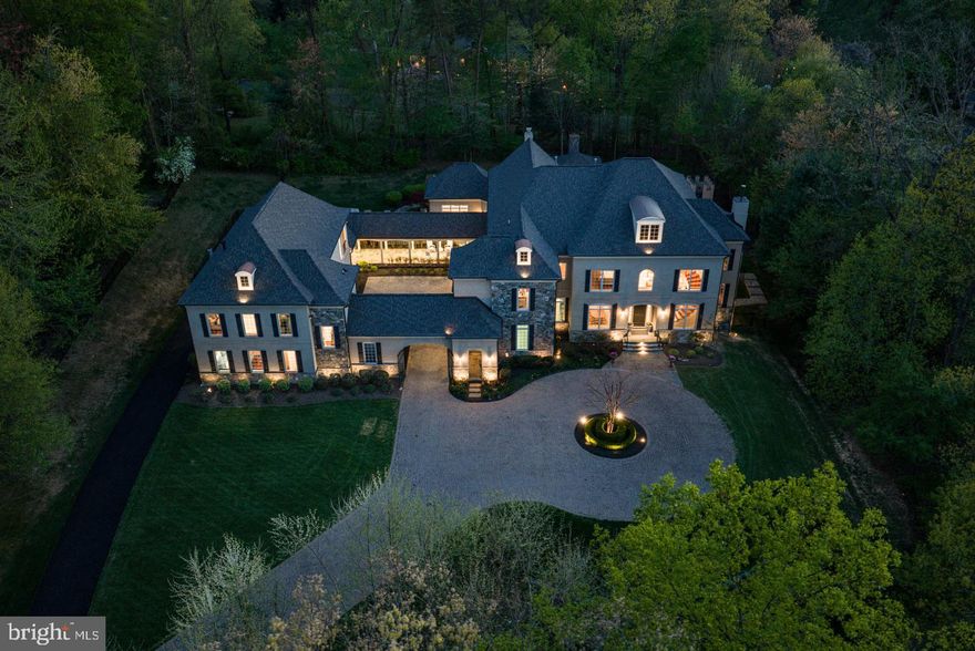 Gracefully positioned at the end of a private cul-de-sac on 2.12 manicured acres, this exceptional French Country estate with a private guest house and resort-style pool offers timeless elegance along the coveted Great Falls–McLean border within the Langley High School pyramid. Built by Keswick Homes, the residence spans 13,448 square feet and showcases soaring ceilings, Brazilian cherry hardwood floors, exquisite millwork, expansive windows, and a three-level elevator. A long private drive leads to a motor court and porte-cochère, setting the tone for the home’s impressive scale and craftsmanship. The chef’s kitchen is beautifully appointed with Sub-Zero, Wolf, and Miele appliances, dual islands, custom cabinetry, and seamless flow to the breakfast room and grand great room with a fireplace. Formal living and dining rooms and light-filled gathering spaces create the perfect balance of luxury and livability. The upper-level primary suite offers a private sitting room, fireplace, balcony, dual custom walk-in closets, and a spa-inspired bath. Rounding out the five en suite bedrooms on this level are a primary-size suite and an independent wing of three generously proportioned bedrooms, one with a zero-entry shower with bench seating, extra-wide doorways, and wide hallway access to the elevator, ideal for multigenerational living. The expansive lower level features a media room, wet bar, billiards, recreation spaces, flex rooms, and guest accommodations. Outdoor living is truly spectacular with a 20x40 heated saltwater pool, retractable cover, outdoor kitchen with Viking appliances, stone fireplace pavilion, and over 6,000 square feet of Pennsylvania bluestone patios and covered porches. A detached 3,000+ square-foot carriage house includes its own kitchen, family room, two bedrooms, and a commercial-grade gym, creating an ideal guest residence, wellness retreat, or multigenerational living environment. Moments from Tysons, McLean, and Washington, this extraordinary estate offers privacy, scale, and resort-style luxury in one of the region’s most prestigious settings.