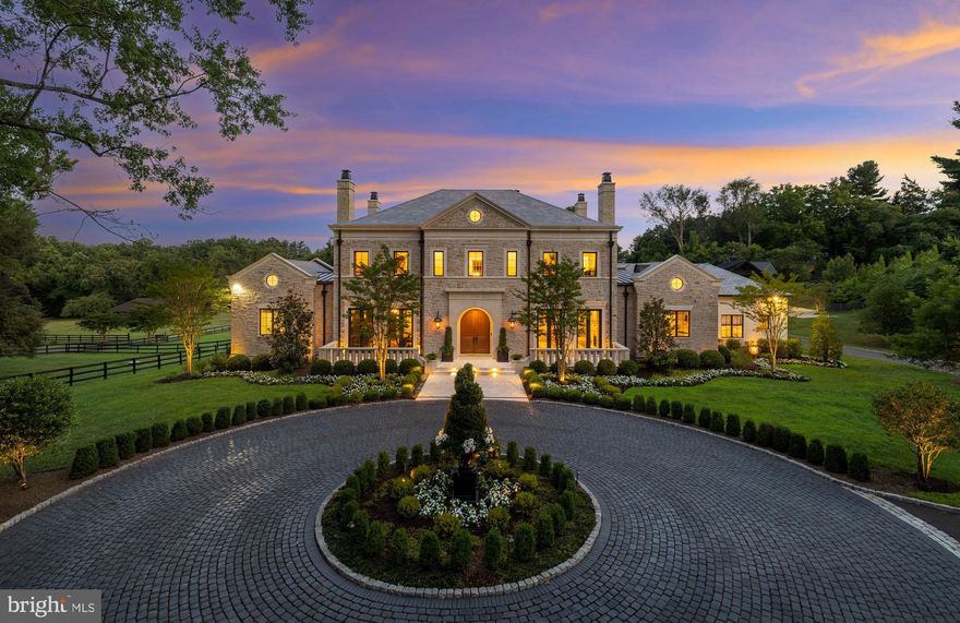 Wrought-iron automatic gates open to reveal a meandering driveway leading to a cobblestone circle, upon which stands one of the Capital Region’s finest residences. Built by Sugar Oak and designed by master architect Mark Hughes, AIA with Harrison Design, 1209 Towlston is the product of a premier collaboration, offering both luxurious living and exceptional equestrian facilities.
 
Clad in rough-cut stone, the exterior resembles a Tuscan country estate. Verdant landscaping surrounds an intricate arched limestone entrance. Solid wooden double doors part ways to reveal a stunning rotunda with gleaming marble flooring and an artistic chandelier illuminating the space from above. Designed with a thoughtful floor plan, the main level comprises a blend of resplendent formal rooms and relaxed, informal spaces. The twelve-foot ceilings, quadruple-hinged 1¾-inch doors with crystal hardware, wide moldings, baseboards, and recessed spot lighting throughout the main level showcase the meticulous attention to detail and high-quality craftsmanship invested in the construction.
 
A coffered ceiling and arched floor-to-ceiling windows flood the grand central living room with natural light. The formal dining room, lined with splendid floral wallpaper, can be discreetly closed off from the greeting area via pocket doors. Softly lit integrated bookcases, an intricate ceiling, and one of six roaring fireplaces create a sophisticated atmosphere in the formal library. Within the informal areas, a casual family room directly accesses the covered terrace and faces the chef’s kitchen. An 18-foot beamed cathedral ceiling highlights the scale of the chef’s kitchen, complete with a thick-edge marble island, and commercial-grade Blue Star, Fisher & Paykel, Thermador, and Sub-Zero appliances. A butler’s pantry adjoins the dining room, combined with smoked mirrors and open shelving. An extensive mudroom with pet wash and laundry facilities connects to the double-height four-car garage.
 
On the opposite wing of the main level, double doors part ways to reveal a chic sitting room with a wet bar leading to the primary bedroom suite. ​​The luxurious suite overlooks verdant greens through a curved wall of windows, replete with a sumptuous marble bath and two dressing rooms, each with extensive custom shelving. Upstairs, four generous bedrooms overlook the main foyer, each featuring a built-in desk and walk-in closet; two are ensuite, and two share a Jack-and-Jill bath. The upper level is complete with convenient laundry facilities.
 
Designed for entertaining, the lower level features a full kitchen with integrated wine storage and bar seating, as well as a large walkout recreation room. A fitness center, spa bath with a steam shower and sauna, and a sixth-bedroom suite complete the space.
 
The covered patio affords separate access to a thoughtfully designed pool bath and changing room. Stepping down from the loggia is an expansive travertine patio housing the 40-foot heated pool with an electric cover and a full outdoor kitchen. Out back, five acres provide ample space for extensive equestrian facilities and incredible riding space. The comprehensive onsite horse barn contains five stables, a tack room, a separate sitting room, and a half bath, as well as a sweeping unfinished upper level with a vaulted ceiling. Behind the scenes, industrial-grade systems such as extensive Sonos and Lutron audio and visual automation, security video surveillance, and the latest in HVAC and water treatment technology create a fortress of luxury. Situated in close proximity to Washington yet filled with an overwhelming sentiment of tranquil seclusion, 1209 Towlston stands as an emblem of lavish countryside living, establishing itself as one of the Capital Region’s finest residences.