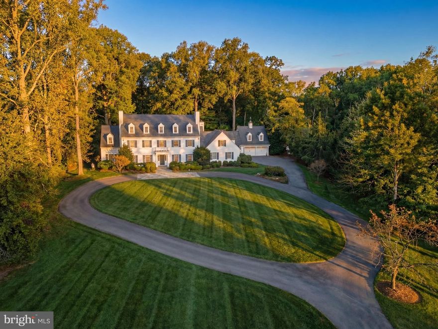 Tucked away behind the nationally-renowned Congressional Country Club, its namesake Country Club Drive is one of Bethesda’s most prestigious streets, with a mere 26 of the very finest estate homes dotted along sweeping curves in a picturesque setting. Within this rarified air, set far back from the street on a magnificent, verdant two-acre lot, is this quintessential custom built estate home, originally constructed for its discerning owner. 
Approached by an elegant circular driveway, the white brick and siding facade capped by a synthetic slate roof evokes cues of classic old-world New England colonials situated on large swaths of land, exuding an ethos of quiet luxury. Traversing the portico and mahogany front door framed by intricate transom windows reveals a classic foyer with a prominent grand staircase. Exquisite millwork and wide plank oak flooring set the tone for a refined atmosphere of warmth and sophistication.  
Formal living and dining rooms flank the reception area in a traditional center hall layout. Both spaces are generously proportioned for large scale gatherings, and each feature a roaring fireplace, two of six in the home, along with stylish accent lighting. The latter features built-in china displays while the former flows into a richly paneled library, boasting another fireplace, bridging both living and family rooms. An ethereal space as a byproduct of double sets of French doors opening onto the rear patio, the family room’s coffered ceiling and stone fireplace inject intimacy into an otherwise substantial room.
At the heart of the home’s informal area is the award-winning chef’s kitchen, fully reimagined by Jack Rosen Custom Kitchens to blur the lines between aesthetics and function. Bright white shaker cabinetry contrasts with dark-stained hardwood floors, while the thick, honed Carrara marble island top does the same with stunning leathered granite perimeter counters. A spectacular custom stainless-steel hood is the centerpiece, while a comprehensive suite of Wolf and SubZero appliances represents the top-of-the-line in commercial grade equipment. The adjoining butler’s pantry has been reimagined with lighted glass-front cabinetry and a wine fridge, effortlessly bridging the transition to the dining room. An adjacent keeping room with fireplace and sunlit breakfast room with paneled cathedral ceiling bring the outdoors in. The main level is thoughtfully completed with a spacious mudroom, featuring extensive built-in cabinetry and an adjoining full bathroom, providing a practical yet refined conclusion to the main level. 
The upper level primary suite occupies a dedicated wing. Featuring a large bedroom with access to a private covered terrace, as well as a sitting room with a breakfast bar tucked away behind French doors, the space is a secluded retreat of opulence. The sumptuous bath features all of the ubiquitous spa-inspired amenities, including a jetted soaking tub, and the dressing room is lined with custom built-ins. Four secondary bedrooms and three baths are found on the upper level, while the top level loft can serve as an additional bedroom or multipurpose space.