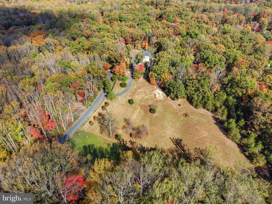 Welcome to 13025 Yates Ford Road — nestled on five acres, timeless craftsmanship meets modern luxury in the heart of Clifton. From the moment you step through the front doors, you'll feel the home's inviting elegance. The soaring two-story entryway, detailed wainscoting, and exquisite crown moldings set the tone for what lies ahead: a residence where architectural detail and comfort coexist in perfect harmony.

The great room, framed by a dramatic coffered ceiling and two stories of sun-drenched windows, flows seamlessly into the gourmet kitchen — the heart of the home. Here, exposed wooden beams add warmth and character above a well-sized island with breakfast bar seating, while the morning room invites you to linger over Sunday pancakes and waffles with sunlight streaming in.  The kitchen features a chef-inspired kitchen with a Wolf Sub-Zero appliance suite and a walk-in pantry for all the ingredients!

An upper-level loft overlooks the great room below, creating an open, connected feeling throughout the home. The main level also offers both formal and casual spaces — a dining room for special gatherings, a refined sitting room for quiet conversations, and two versatile flex rooms that adapt effortlessly as a main level bedroom or dual home offices. A full bath, powder room, and mudroom off the three-car garage complete the thoughtful main level design.

Upstairs, the primary suite is a sanctuary of sophistication. Through double doors, a tranquil sitting area and double-sided fireplace welcome you to unwind beneath tray ceilings. The spa-inspired ensuite features dual vanities, a newly added soaking tub, and an expansive walk-in shower — complemented by two generous walk-in closets. Three additional bedrooms each include their own private ensuite bath, with the added convenience of an upper-level laundry room.

The fully finished lower level is designed for both relaxation and entertainment — complete with a wet bar and wine fridge, spacious recreation area, fitness studio, a fifth bedroom, and a full bath. Step outside to your private backyard retreat featuring a built-in hot tub and fire pit — perfect for al fresco dining, evening stargazing, or cozy bonfires beneath the trees.

Set on a tranquil, tree-lined lot, this home offers luxury living that feels grounded, welcoming, and deeply personal. The Historic Town of Clifton exudes small-town charm reminiscent of a quaint countryside village, yet you're just moments from modern conveniences, scenic parks, and Paradise Springs Winery — and less than an hour from Washington, D.C.

13025 Yates Ford Road is more than a home — it's a place where every space tells a story, and where every day feels just a little bit extraordinary. Mortgage savings may be available for buyers of this listing.