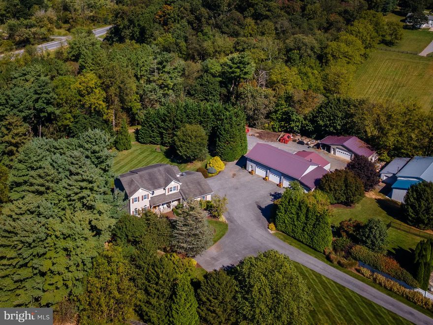 Set on over 4 acres in Finksburg, this impressive, one owner, custom-built colonial with 3-bedrooms and 3.5-baths features upgrades and special finishes throughout, paired with impeccable landscaping and hardscaping for an elevated lifestyle, both indoors and outside. Outside, you'll find large detached garages (one is 35x52) with various overhangs and spaces perfect for parking, storage, and workshop use. This lovingly maintained and curated property is perfect for an at home business or vehicle enthusiast! The backyard is designed for every season with an expansive deck, patio with custom stone hearth, and mature landscaping, all tucked away at the end of a long private driveway and no neighbors in sight. The oversize 2 car attached garage is finished with plenty of storage and workbench space. There is also separate, secure office access right next to the garage entrance. Just inside the peaceful front porch you'll step into a foyer, with a living room immediately to your left with brand new carpeting, and a large formal dining area or additional study to your right with gleaming hardwood floors. The open-concept rear of the home features a spacious living room with stone hearth and propane fireplace, vaulted ceiling open to the catwalk upstairs, and open flow to table space and a sliding door entrance to the composite decking scaling the back of the home. The large, well appointed kitchen features a stone floor, center island, stainless appliances, ample custom cabinetry, updated lighting, a pantry, granite countertops, and access to the stairs, powder room, mud room, office, and garage. The office has a ceiling fan, closet, hardwood flooring, and exterior access, but could easily be converted into a first floor bedroom. The main floor has a perfect open feel while still maintaining separate spaces where necessary. Upstairs, the spacious and impressive primary suite features a vaulted ceiling, full bath with skylight and separate walk-in shower and jetted tub, water closet, updated dual vanity and walk-in closet. Two other large, bright bedrooms and a full bath with tub/shower combination complete the second floor. The basement is completely loaded with many custom features and touches and is the ultimate play space! The family/game room features a custom stone fireplace (yes, that is a real boulder!), wet bar with cabinetry and custom counter, and a full bath downstairs with unique vanity and copper sink. A custom train track runs the perimeter of the room! There is an additional finished space with built in wine racks, safe, and lighting. The basement also features a walk-out to the excellently detailed and appointed yard space, full of custom hardscaping, stone work, and landscaping. This property provides a true retreat and easily shows how well thought out everything has been since the day it was built. The multiple garages and outbuildings all have electric and the back shop also has plumbing. This property provides endless opportunity for an at home business, whether you are a contractor, landscaper, automotive industry... or whatever your hobby or career demands! Mature plantings and strategic foliage and flowers surround the property, from the bridge over the water feature and pond with seating area to the cherry trees along the driveway, providing multiple tranquil outdoor spaces. This type of privacy in such a desirable location, combined with so many outdoor amenities for garage space, storage, and a custom built home does not come along often. 3889 Gamber Rd is truly a special property with limitless offerings to its next owner!