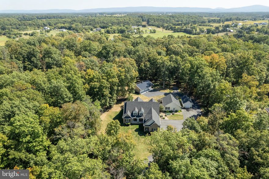 Set on just under 5 private, tree lined acres, this exceptional home offers space, flexibility, and a layout designed for both everyday living and multi-generational needs.

A welcoming front porch leads into a beautifully designed interior featuring a stunning two-story family room filled with natural light and overlooking views from the upper level. The main level offers a spacious primary suite complete with an updated bath, creating a comfortable and convenient retreat. You’ll also find a dedicated home office, formal and casual living spaces, and a bright breakfast room as well as a covered porch with a patio in the back, perfect for morning/evening gatherings.

Upstairs, two generously sized bedrooms each feature their own private full baths, along with a large bonus room, ideal for a media room, playroom, or additional living space in place of a basement. An open sitting area overlooks the family room below, adding to the home’s airy and connected feel.

One of the standout features is the full in-law suite, thoughtfully designed with its own private front entrance and an entrance via an enclosed hallway from the main house. This space includes two bedrooms, two full baths, a full kitchen, living room, and laundry, perfect for extended family, guests, or potential rental use.

Car enthusiasts or those needing extra storage will appreciate the extensive garage space, including an attached 3 car garage, a separate 1 car garage for the in-law suite, and an additional detached 3 car garage.

Surrounded by mature trees for added privacy, this property offers the perfect blend of peaceful country living with room to grow, gather, and entertain.
