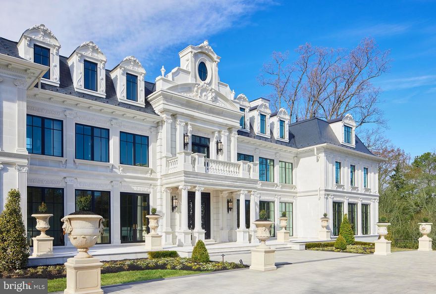 Timeless architecture, unparalleled scale and one of America’s most prestigious addresses in McLean, Virginia just minutes from Washington, DC. 6431 Georgetown Pike encompasses nearly 4 acres and spans 22,000 square feet across 4 levels with 10 ensuite bedrooms. French design has made a significant impact in the United States, particularly in the Washington D.C. region, Palm Beach, Bel Air and Beverly Hills, reflecting classic elegance and sophistication. A sweeping private drive leads to stately wrought iron gates revealing a breathtaking approach to the center of the home within a large motor court. Captivating iron work carries through to the double front doors. It’s a first impression that radiates enduring sophistication that transcends trends. What you’ll find inside this Langley Farms home are interiors designed for modern living at the highest level. A gleaming Italian marble foyer offers front-to-back views from the moment you enter. Exquisite floor-to-ceiling millwork, white oak hardwoods and hand forged iron railings are thoughtfully integrated throughout the home, creating a subtle continuity reflecting the highest quality craftsmanship and design. An oversized living room is tailor made for large scale entertaining as well as intimate gatherings featuring full height windows with panoramic garden views, a wet bar and a trellis plaster ceiling. The graceful moldings are showcased across the main level including the dining room currently set for 12 guests, a handsome paneled fireside library, and a coffered ceiling in the great room. The principal kitchen features multiple satellite work areas, including an adjacent catering kitchen and butlers pantry. The second level primary bedroom retreat spans an impressive 3,300 square feet, with it’s own sitting room and a private terrace, each elegantly appointed with fireplaces. The suite features a double vanity bathroom with a standalone soaking tub as a central design component, and a spacious shower, enveloped in beautiful tile work and luxurious fixtures. An extraordinary two-story primary bedroom closet redefines luxury, showcasing top-of-the-line Italian cabinetry meticulously crafted to optimize space and style. Every detail invites homeowners to display their wardrobes and accessories in an elegant, thoughtfully designed environment. The builders are offering an opportunity to add an additional two-room closet with kitchenette and full bathroom by seamlessly incorporating a passageway from the bathroom into the currently designated separate second-floor apartment. The second level includes 3 elegantly appointed ensuite bedrooms, and the third level also features 3 ensuite bedrooms. The lower level offers 2 more ensuite bedrooms, ensuring privacy and ample accommodations for large families, guests and staff, with each floor thoughtfully equipped with its own kitchen and laundry room. The lower level is a spectacular haven for leisure, featuring a tiered screening room, a dedicated spa with dry sauna and steam room, a wellness relaxation room, a massage room, a glam room, a gym, and a stylish lounge with a gracefully contoured wet bar and direct access to a private outdoor area that beautifully mirrors a serene park setting. The rear grounds are anchored by a swimming pool adorned with elegant waterfall and fountain features, complemented by a floor to ceiling waterfall. This outdoor retreat also features a retractable 200 inch television, and a covered dining area with a built-in grilling kitchen. Behind the scenes, the entire property is self-sufficient with smart home technology controlling lighting, sound, HVAC and security systems. The residence includes 5 deep garage bays and enough secure hardscape for 30 cars. Additionally, furnishings can be included in the purchase offering an attractive opportunity for an effortless transition. 6431 Georgetown Pike showcases meticulous craftsmanship, infusing warmth throughout and accentuating its classic beauty.
