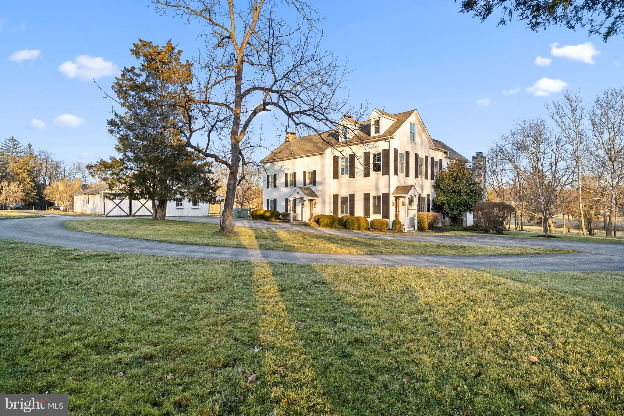 Introducing 3 Mill Road, situated in the midst of Radnor Hunt country where you’ll enjoy rolling hills and scenic vistas! This beautifully preserved historic property is brimming with charm and offers modern amenities for today’s buyer. With picturesque views and a babbling creek along the boundary, this wonderful property features a main house, a springhouse, a tidy wood shed, and a barn with stalls, tack room, garden room, and upper-level party room! Tucked away at the end of a quiet road in Great Valley School District, this amazing home is truly one of a kind. Unique details abound – deep windowsills, decorative millwork and moldings, cherry and walnut hardwood floors, exposed beams, shiplap, and multiple fireplaces.
The circular driveway offers plenty of parking and guides you to the both the front and side entrances to the home. Enter the front door and you are welcomed into the “farmhouse room” with its gleaming hardwood floors, overhead beams, huge fireplace with wood burning stove, and access to the private and covered rear porch overlooking the beautiful grounds. To your right, and adjacent to the side entrance with spacious foyer, is the fabulous gourmet kitchen that opens to the light-filled breakfast area and stunning great room. The kitchen boasts high ceilings, recessed lighting, massive center island with seating, granite countertops, stainless steel commercial grade appliances, white custom cabinetry, pantry, and farmhouse sink. French doors from the kitchen open to the cozy porch and large patio with outdoor fireplace – perfect for al fresco entertaining or just enjoying the views with your morning coffee! A beautiful coffered ceiling and gas fireplace with mantel highlight the spacious great room, and from here a second set of French doors grants access to the rear yard. This level is completed with a powder room and coat closet. Ascend the wide staircase to the second level where you will find two bedrooms, each with a decorative fireplace, a tiled hall bath with pedestal sink and tub/shower combo, and a linen closet. Just a few more steps take you up to the next landing and the expansive primary suite with vaulted ceiling, French doors to a balcony, spa-like primary bath with oversized glass stall shower, separate vanities, private toilet, clawfoot soaking tub and linen closet. Adjacent to the primary bath is the walk-through primary closet with plenty of daylight, storage space, and conveniently connected laundry area. The upper level offers a loft area – perfect for hanging out or home office, plus a small study area, two additional spacious bedrooms (one with decorative fireplace) , hall storage, and a shared tiled bathroom with stall shower.
The outdoor space is perfect for year round fun offering a cozy fireplace for the cooler months, barn with stalls, one car parking and finished second floor to host parties, and the charming springhouse that was renovated for a private oasis.
Close to many top private academies, downtown Wayne and Malvern Borough, and easy access to all major roadways for an easy commute to Philadelphia, Wilmington, and NYC. This amazing property is a rare find in the desirable Radnor Hunt area – call today for more information or to schedule your showing!