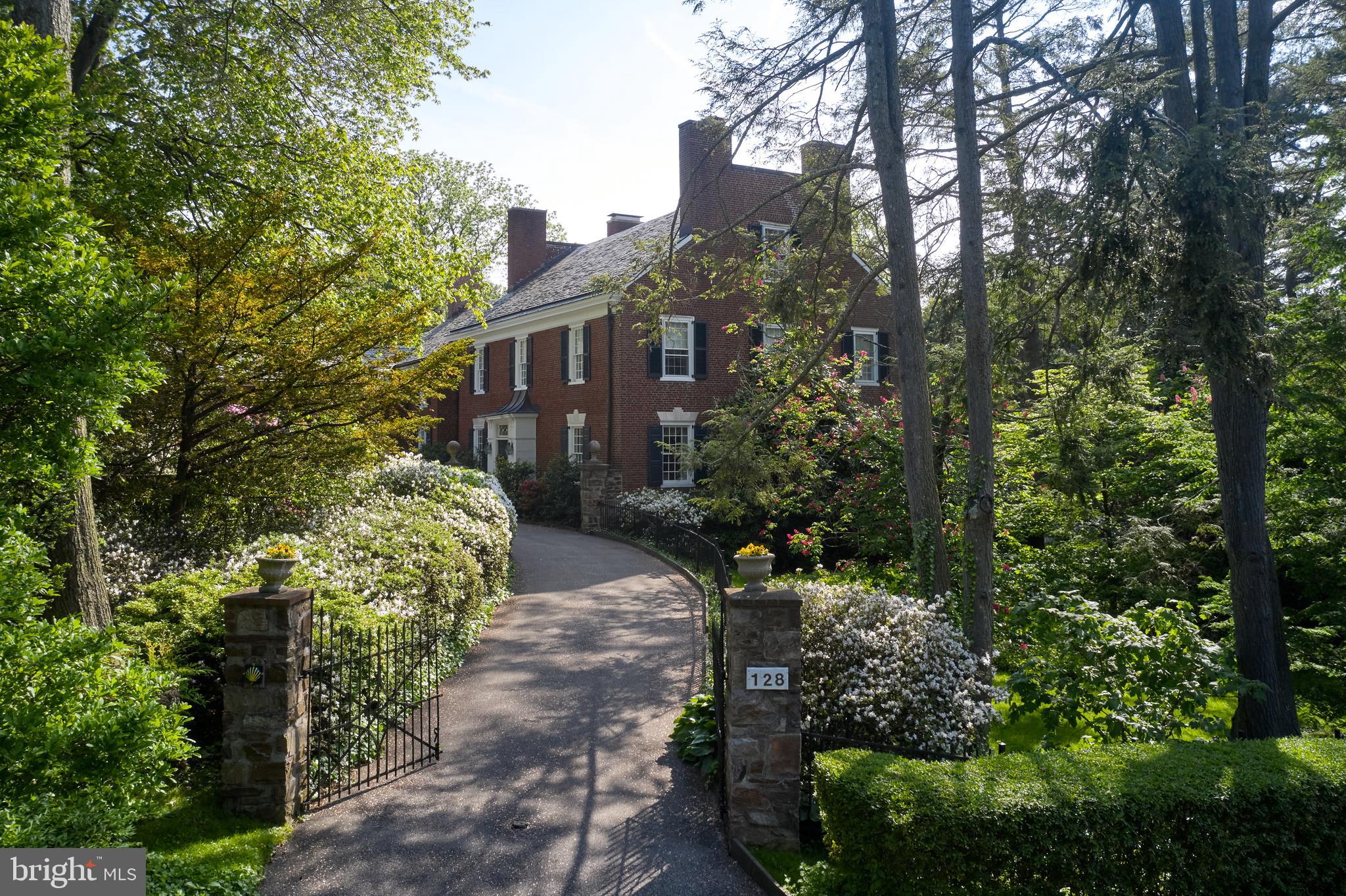 Set behind a gated entrance, you enter a beautiful stone-walled front courtyard enhanced by flowers and an intimate fountain. This home has all the sophistication and class of the finest estate homes on the Main Line. In 1928, it was designed and built in the spirit of Horace Trumbauer’s last great estate, Ardrossan, for the Montgomery family. As with Ardrossan, this home is an outstanding example of early 20th-century Georgian-style architecture and is a refreshing oasis with 1.02 acres of property and a deeded additional lot of .49 acres which with an acceptable offer the buyer of the main house
will have first right of refusal. This is all located in the heart of the Main Line suburbs. This brick residence has a commanding, stately presence, with many design elements rooted in classical architecture. There have been newer additions for today’s living: An enlarged kitchen, informal dining room, and family room that blend seamlessly with the magnificent structure and its old-world features.
Upon entering, the bright reception foyer runs front-to-back and front-to-side and is trimmed in rich millwork and built-in bookcases, with black and white parquet floors and a lovely stairwell. To the right is a formal living room with fireplace, random width and length wood flooring, multiple seating areas, plenty of large windows, and a wall of paned glass with French doors to a step-down, awninged, Pennsylvania stone terrace that leads across to a terraced stoned dining area. Terraces run along almost the entire length of the back of this home. To the left of the living room is the formal dining room with fireplace, same wood flooring as the living room, and includes a lovely garden mural painted by the famous faux artist Carroll Barnes with four floor-to-ceiling built-in corner cabinets plus secret side panels for more storage. The kitchen is a chef’s dream. In addition to the original kitchen, it now has an ample-sized, wood cutting board island, stainless steel appliances including a Viking gas range, a wet bar area, an ice maker, and plenty of natural light. Adjacent to the kitchen is an addition of a lovely informal dining area with high ceilings and wall of windows and glass French doors to the pergola-covered terrace. There are wide, beautiful stone stairs from each terrace to access the grounds and pool.
This home’s private quarters include two ensuite bedrooms on the 2nd and 3rd floors, and two more bedrooms on the second-floor main house, which share one hall bathroom. The main suite is spacious and comfortable with a fireplace, sitting area, balcony, walk-in closets, and his and her bathrooms. A study/office is part of the main suite. Across the hall from the main bedroom is a ladies’ dressing room with a wall of closets for additional storage. The additional two bedrooms on the second level are all generously sized and feature views of the grounds. There are back stairs off the second-floor hall from the study/office and the mud room area on the first floor. These stairs connect the main house to three more bedrooms and a bath above the porte cochere and three-car garage. On the 3rd floor over the main house, there’s an additional en suite bedroom and large attic providing additional storage.
This home has lush plantings and a verdant lawn. A delightful wildflower meadow is behind the home, with a charming old stable used as a shed and a giant dollhouse just for fun.
This home is the complete package offering privacy, fabulous quality construction, and a long list of updates to create a modern, comfortable home. The property is near the Villanova College campus, has countless dining and shopping options, medical offices, and hospitals, is close to public transportation and interstate highways, and is located in the award-winning Radnor School District. Don’t miss this fabulous opportunity!