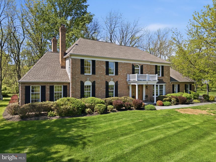 Nestled on a private wooded lot backing to a tranquil stream, this gorgeous brick Colonial offers timeless elegance and exceptional privacy, all within beautifully manicured grounds. A long, sweeping tree-lined driveway welcomes you home, while mature landscaping and meticulous lawns create a stunning first impression. Follow the bluestone pathway to the covered front entrance and step into the grand two-story foyer, where gleaming hardwood floors and a dramatic winding staircase set the tone for the sophisticated interior. Elegant picture frame wainscoting flows throughout the foyer, formal living room, and dining room, creating a refined atmosphere ideal for entertaining. The formal living room features a beautiful gas fireplace with a classic brick surround, while the adjacent first-floor office offers custom built-ins and an exposed brick accent wall, providing both warmth and character. The well-appointed kitchen is designed for both everyday living and entertaining, featuring abundant hardwood cabinetry, a center island for casual dining, custom finishes, extensive tile backsplash, double pantry, and high-end appliances including a Sub-Zero refrigerator, double wall ovens, and a built-in wine fridge in the beverage area. A bright, bumped-out breakfast area overlooks the serene wooded backyard, bringing nature indoors year-round. Flowing seamlessly from the kitchen is the spacious family room, complete with a cozy wood-burning fireplace and stately stone mantle. The sunroom is a true showstopper, featuring exposed brick and walls of windows that showcase breathtaking views of the expansive, private backyard. Completing the first floor is a dedicated laundry room, powder room, and convenient access to the attached three-car garage. Upstairs, solid wood flooring extends throughout all four bedrooms. Three generously sized bedrooms share a hall bath, while the luxurious primary suite offers a private sitting room, two oversized walk-in closets, and a spa-like ensuite bath complete with a soaking tub and skylight. The finished basement adds incredible versatility with durable LVP flooring, abundant storage space, and the potential for an additional bedroom, gym, or recreation area. Outside, enjoy peaceful outdoor living on the large composite deck that steps down to a paver patio and walkway, complete with a hot tub for year-round relaxation. The massive backyard offers exceptional privacy and endless possibilities for entertaining, play, or simply enjoying the natural surroundings. Ideally located for commuters, this exceptional home is just minutes from I-295 and close to Yardley and Newtown, offering easy access to acclaimed restaurants, boutique shopping, and year-round community events.