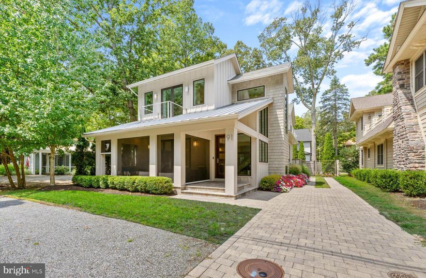 Step into this beautifully crafted, gently lived-in home that seamlessly blends modern luxury with thoughtful design. Ideally situated to overlook serene wooded parklands, this stunning residence features a welcoming front porch and sleek architectural lines that immediately impress! Inside, the open-concept floor plan offers an effortless flow between living, dining, and entertaining spaces. The expansive living area opens to a tranquil screened porch complete with retractable screens, while the sophisticated dining space includes a wine fridge, built-in storage, and a wet bar—perfect for hosting gatherings. The chef’s kitchen is a true showstopper, outfitted with commercial-grade appliances, including a Sub-Zero refrigerator, Wolf 6-burner range with double ovens, warming drawers, and a spacious prep island. The main level also features a luxurious primary suite with a spa-inspired en-suite bath and a custom walk-in closet. Just down the hall, a well-appointed laundry room offers ample storage and a convenient utility sink. Upstairs, guests will enjoy four generously sized bedrooms and three beautifully designed, spa-like bathrooms. A large sun deck provides the perfect spot for relaxing or sunbathing in privacy. The rear yard and outdoor space is an entertainer’s dream, complete with a built-in grilling station, pizza oven, and fully fenced yard for added privacy and charm. In addition to its elegant living spaces, the home also includes a full basement offering a second laundry area and abundant storage – perfect for keeping beach gear, seasonal décor, or anything else you need tucked away yet easily accessible. Located just blocks from the beach, public tennis courts, and the vibrant shops and restaurants of downtown Rehoboth, 91 Columbia offers the ideal combination of luxury, location, and lifestyle. If you’re searching for an exceptional beach home, your search ends here.