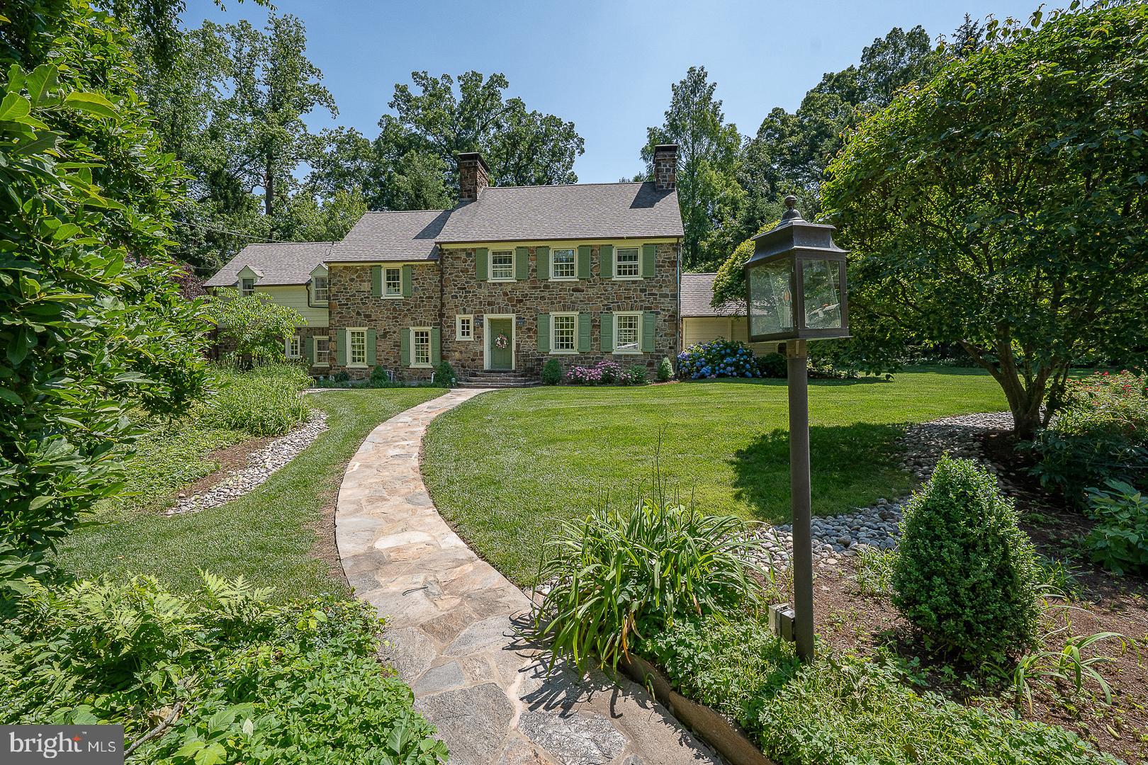 Stately and beautiful, all hand-cut stone center hall colonial, sighted on an idyllic one acre lot with forested front lawn, located on one of the premier streets in Lower Merion. Architect John Lane Evans won multiple awards for his design, completed here in 1936. Radial stone steps up to portico and front door. Entrance foyer and center hall has coat closet and is 'straight thru' to back door, with stairs and powder room. Elegant, formal living room has prominent stone fireplace with a flagg hearth and built-ins with custom paneling. Cozy hideaway Library / Den lies beyond the LR, with second fireplace, custom paneling and built-ins. Den has bright and sunny glass atrium door for rear lot egress, and a charming water feature. To the left of the Foyer and center hall, step down into the formal dining room, with a third fireplace, built-in china cupboards and a modern, glass window wall at the back, that opens to a private stone patio with electric awning. All of the formal rooms and foyer on the first floor have gorgeous and elegant random-width, hand-pegged hardwood floors. Dining room opens to both the Butler's pantry with sideboard and sink, and upper cabinets for glassware, and separately, opens directly into the cook's Kitchen, back stairs and breakfast room. Eat in kitchen has breakfast nook, custom lighting, Corian counter tops with peninsula and sink at the side window. Double wall ovens, dishwasher and cooktop with custom tile backsplash complete the room. Rear kitchen glass vestibule has back door to stairs, garage and driveway. Just off the Butler's pantry is a full bathroom and separate 4th family bedroom, currently in use as a WFH office.
Main stairs up to second floor landing, with hardwood floors throughout. Spacious owner's bedroom suite has large walk-in closet and 'retreat' sitting area. Bedroom is sunny and bright with six pretty windows, and has a full, private bath. Two additional, spacious family bedrooms share a second, full hall bathroom. Hall has additional linen and storage closets, along with back stair access.
Partial lower level is at grade, with 1.5 car attached garage, full laundry room with walk out to covered alcove and driveway and storage or play room with mechanicals. Whole house natural gas generator.
