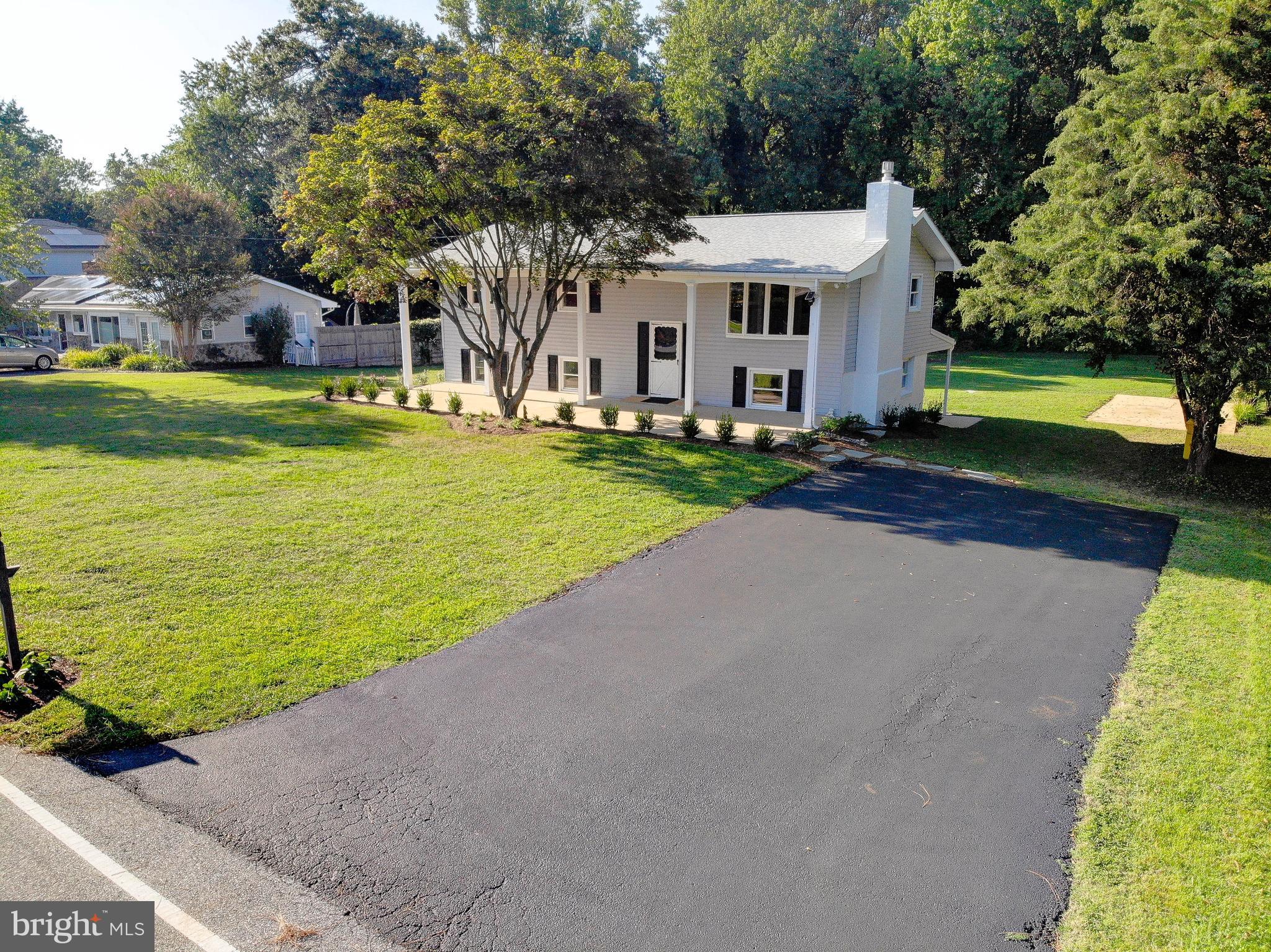 Welcome to this 4-bedroom, 2-bath split foyer located in the charming waterfront community of Holly Hill Harbor. Nestled among stately waterfront estates, the home offers partial water views of the Rhode River along with additional lots (1/2 of 58, 59, and 60 on Dogwood Road), bringing the total property size to nearly 0.73 acres (31,974 sq. ft.). These extra lots provide added space and privacy backing up to a quiet wooded area. The home greets you with excellent curb appeal, featuring an inviting front porch, and has been freshly painted inside and out. Relax on the porch while watching peaceful water glimpses, or host gatherings on the expansive covered back patio. Inside, the main-level living room boasts a wood-burning fireplace and a large bay window that frames the partial water view. The kitchen includes stainless steel appliances. On the lower level, a spacious recreation room offers a second fireplace with a propane gas insert, new luxury vinyl plank flooring, and a slider that opens to the covered patio—perfect for indoor-outdoor entertaining. This property is part of an estate sale and is being offered in AS-IS condition, though it has been very well maintained and is move-in ready. Enjoy access to a community boat ramp for kayaking or boating, and the concrete pad in the large back yard can store your boat after a long day on the Chesapeake Bay.