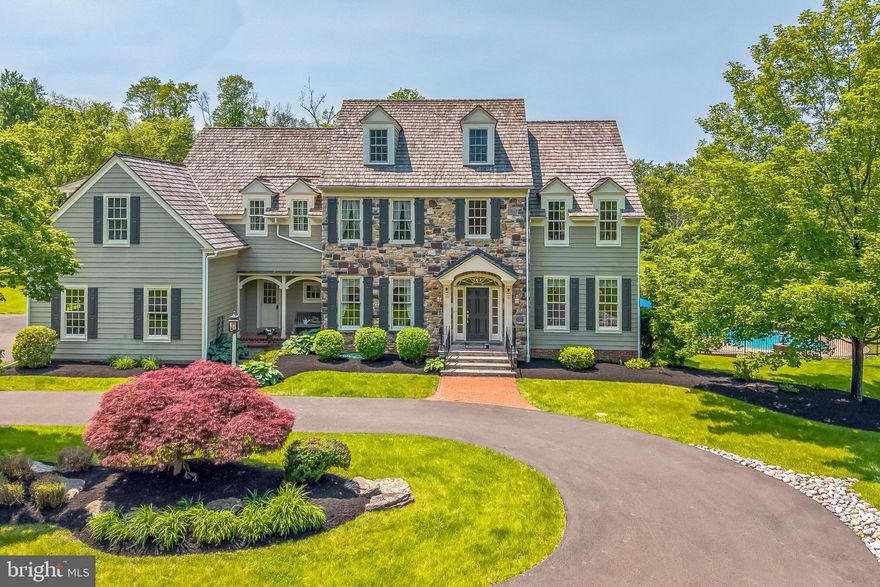 The Andrew Downing house is a farmhouse reproduction built by master craftsman Bruce T. Lesser in 1998. This home is situated in Upper Makefield at a location that is steeped in history and surrounded by over 150 acres of preserved open space.
Adjacent to London Purchase Farm, across the road from the Revolutionary War hospital (Antrobus Farm) and abutting the open space of Tory Ponds and Doan Hollow, this location is filled with wildlife and peaceful serenity.
This home offers three levels of living space, along with a stairway to a fourth level. The stately front entrance is flanked by custom woodwork and lanterns. The tall dining room windows face the circular driveway, giving a welcoming feeling to family and guests. Ceiling medallions are prominent in the home. The formal living/music room has a coffered ceiling that supports the acoustics of the 9 foot ceilings.
The main floor study has built-in shelves and cabinets with a double pocket door to the living room and a glass French door to the back hallway. The family room has a 9 foot ceiling that cascades to 14 feet at the gas fireplace with custom  over mantle. The fireplace is framed by two tall windows with plantation shutters overlooking the spring house in the back yard. A private balcony is accessible from the family room through a double French door where the beautiful sunset can be appreciated.
The kitchen suite includes an eating area with a wall of windows, open access to the family room, double French doors to a covered porch and a gathering space. The kitchen boasts hand crafted fruitwood cabinetry, new granite countertops, center island, dry beverage bar, a convection oven and microwave/oven and a sub zero refrigerator.
The mud room/drop zone is off of the kitchen with access to the front porch, garage & laundry area. The laundry room has a newer washer/dryer and a folding/hanging system. There is a utility sink in the laundry room where you can wash up after a day in the perennial gardens.
Pocket doors are in the kitchen and laundry access to the mud room to provide a safe haven for family pets.
The second floor has 4 bedrooms (2 are ensuites) and a 2nd floor home office. The main bedroom has a large future closet with a new rolling custom barn door. This bedroom area has 6 windows (front, side & back breezes are calming) and Bowman’s Tower illumination can be enjoyed each year.
The second en-suite bedroom has windows on every side, a locker room style walk in closet and Mercer tiles in the shower.
From the second level, there is access to a staircase leading to the attic. Storage galore!
The lower level is a finished climate controlled 1900 foot space with double French doors to a patio and resort style pool, including a spa, easy entry  and several safety features. A gas fireplace is in the lower level living room. There is a full bathroom, eating area, gym area, a workroom, home theater, kitchen and more storage on this level.
There is a storm cellar accessible from the back patio, The home has a full house generator and two newer HVAC units.
This home has been lovingly cared for and is a rare gem!