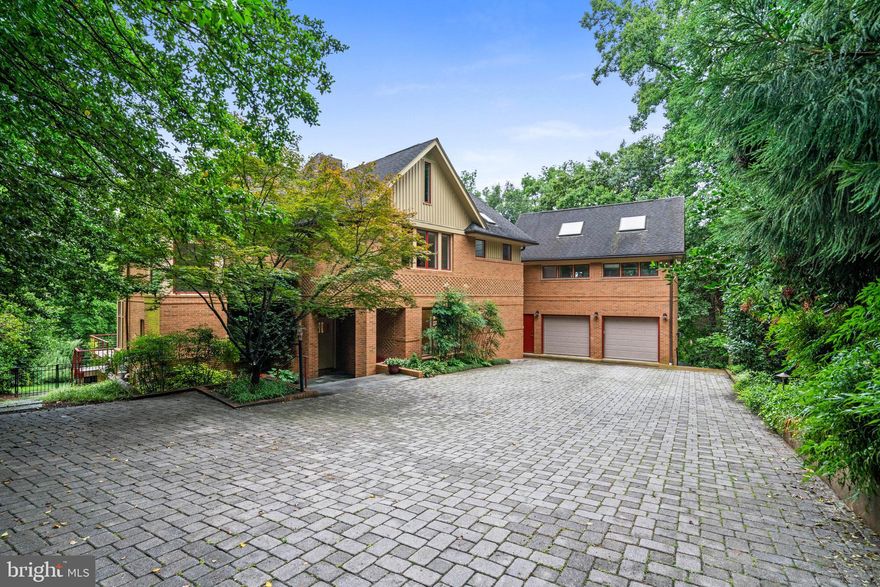 This private residence is sited on over half an acre in the sought-after Forest Hills neighborhood and within walking distance to the shops, restaurants, and the metro in Cleveland Park. It features five bedrooms, plus two additional standalone guest suites, which are ideal for multigenerational living, home offices, art studios or wellness/gym spaces. The home is surrounded by lush landscaping and mature trees and provides a harmonious blend of tranquil seclusion and city accessibility, embodying the natural beauty and quiet appeal that make the neighborhood so distinctive.
Set back from the street, a sweeping gray brick driveway leads to a two-car attached garage and introduces the home with understated style and elegance. Inside, the foyer opens to an expansive living room with beamed ceilings, a stone fireplace, and French doors that open to an oversized deck, filling the room with natural light. The elevated outdoor space provides a serene setting for both quiet relaxation and hosting guests, with panoramic views of the treetops and surrounding landscape. Inside, the main level is thoughtfully designed for seamless everyday living and social gatherings. The gourmet kitchen features stainless steel appliances, including a five-burner stove, double ovens, custom cabinetry, and large windows. It opens directly to a second deck, enhancing the connection between indoor comfort and outdoor beauty. A separate dining room, framed by tall ceilings and built-in shelves, provides an inviting setting for formal gatherings. Also on this level is a study lined with built-in bookshelves and access to the rear yard and deck. A secluded wet bar off the living room adds a thoughtful touch for entertaining.
Upstairs, the primary suite presents a peaceful retreat with high ceilings, a large walk-in closet, and views that evoke a forest hideaway. The spa-like bathroom includes a soaking tub, frameless glass shower, and dual vanities. Three additional bedrooms are located on this level, two of which feature lofted alcoves for additional sleeping or storage space, as well as private balconies. These bedrooms are served by two well-appointed full bathrooms. The lower level includes a fifth bedroom with a fireplace, full bathroom, and walks out to the landscaped gardens. A generous recreation room with built-in shelving and another fireplace is bathed with natural light from French doors that open onto a stone terrace. The level also includes a spacious laundry room with a sink and cabinetry.
This home offers great flexibility with two separate guest or in-law suites. One suite, located off the lower level with a private entrance, includes a kitchen, full bathroom, living room, and its own deck. The second is above the garage, featuring tall ceilings, skylights, and the same full living amenities. 
Outside, the grounds are a sanctuary. The layered landscaping enhances privacy, while a peaceful lily pond and tree-lined views from many rooms deepen the sense of escape. With multiple decks and gathering areas, the home is perfectly suited for both intimate evenings and larger-scale entertaining.
Ideally located blocks north of Cleveland Park and adjacent to Rock Creek Park, Forest Hills offers a unique combination of natural beauty, cultural access, and commuter convenience. Residents enjoy proximity to the Hillwood Estate and Gardens, the National Zoo, and top public and independent schools, along with easy Metro access to downtown DC. This extraordinary property is a unique find, offering the rare opportunity to own a private compound in the heart of Washington, D.C.
