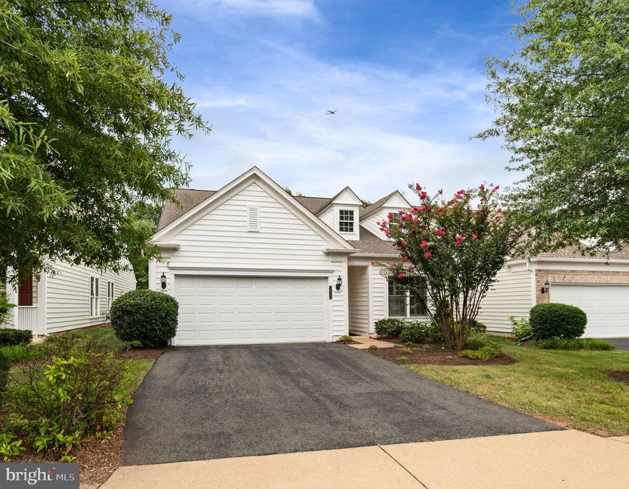 Welcome to this beautifully maintained, light-filled residence offering over 2,450 square feet of thoughtfully designed living space in the sought-after Potomac Green 55+ community. Set in a prime Ashburn location just around the corner from One Loudoun, residents enjoy quick access to Trader Joe’s, a state-of-the-art movie theater, popular restaurants, and premier shopping—all while tucked away in a tranquil, amenity-rich neighborhood.

Step inside to discover scraped hardwood-style flooring throughout the main level (installed in 2023), paired with an open, flowing layout that effortlessly blends comfort and sophistication. The main-level primary suite is a peaceful retreat, featuring a tray ceiling, luxurious en-suite bath with a walk-in shower and soaking tub, and generous closet space.

The spacious kitchen is perfect for everyday living and entertaining alike, featuring white quartz countertops and backsplash, upgraded maple-tone cabinetry, gas cooking, a double wall oven, and a pantry. A pass-through connects the kitchen to the airy dining area, creating seamless flow and natural light throughout.

Also on the main level are a second bedroom and full bath, along with a versatile den or hobby room complete with extensive built-in storage, custom lighting, and a desk—ideal for creative projects or a quiet home office. One of the home’s standout features is the stunning sunroom, which opens through sliding glass doors to a private brick patio with black aluminum railing and peaceful views of the tree-line—a rare and highly desirable feature in this community.

Upstairs, a generous loft provides the perfect space for guests, recreation, or relaxing. A third bedroom with its own full bath and walk-in closet adds even more flexibility for extended visits or multi-generational living.

Additional highlights include an attached two-car garage, proximity to eight guest parking spaces, and easy access to the vibrant community clubhouse, fitness center, pool, walking trails, and a calendar full of clubs and social events.

If you’re seeking a low-maintenance, high-comfort lifestyle in one of Ashburn’s most popular active adult communities, this home offers unmatched privacy, space, and convenience in an unbeatable location.
