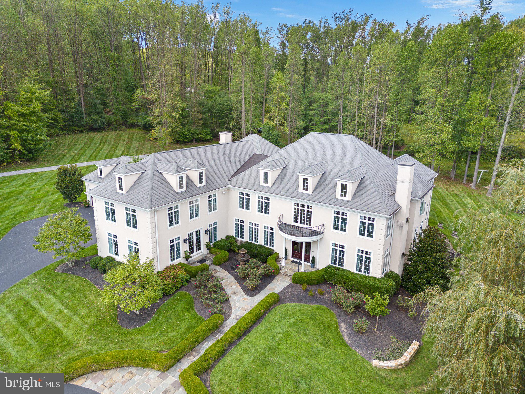 Estate-like serenity awaits in 211 Pumpkin Hill Road. This 6 bedroom 8.5 bath home boasts over 12,600 sq ft of living space. You enter the home through the grand foyer, flanked with a spacious dining room that holds seating for a dozen guests, opulent chandelier pairs, floor to ceiling windows, and rich hardwoods, as well as a large sitting room/living room off to your right. The foyer walks you to the rear of the home where guest quarters are found with a private ensuite and walk-in closet. To the interior of the home you will find the custom kitchen with floor to ceiling cabinetry that is paired in an on trend two-tone color scheme with the large center island(s). The countertops are a neutral colored grain granite that really anchors the space. From the double wall oven to the commercial grade range, no detail has been spared in this chef's dream of a space. A wet bar and wine refrigerator, as well as a breakfast nook, which is currently set for seating for twelve, round out the space. Off of the kitchen you will find the primary family room. This area of the home is inviting and bathed in natural light, while still holding those elevated touches such as the coffered ceilings. From the family room you will enter a hall that holds another bath, and then onto a large private office with separate entrance and walkway from the outside. This executive size office, plus two staff space is ideal for remote workers.
The second level of the home can be accessed by multiple stairways, creating split floor plan access and privacy between the four bedrooms and primary. Let us visit the floorplan from the hall adjacent to the sunroom and office, where you will enter the second level into a beautiful loft/sitting area. All four of the bedrooms in this wing of the home hold ample square footage and closet space, along with their own private ensuites. The convenience of a second floor laundry is also found in this section of the home. through a hallway, flanked by two story access to the lower level, you will find the primary suite. Truly an apartment-like feel in space, this suite holds the owner's bedroom, sprawling seating area, walk-in closet, and private ensuite with soaking tub, stand alone shower, and custom double vanity space.
The home holds an entertainer's paradise, as the lower level is a home in itself. With a full secondary kitchen, billiards room, rec room, family room, office, workshop, sauna, full bath, and steam room, you are left with endless amenities and accommodation in this level of the home.
The expanse of this property brings us to its exterior features. Indoor and outdoor living at its pinnacle, a large stone patio holding two dining spaces walks down to the pool area. Complete with lush landscaping for privacy, this fenced-in area of the yard leads onto the pool house/gazebo which is an ideal outdoor entertainment area that includes a full bath and additional dining patio.
Luxury in a country setting, this estate-like home on Pumpkin Hill holds over 3 acres of professionally maintained lawns dotted with mature landscaping, hardscaping, and gardens. A slice of serenity, yet close to all convenience, 211 Pumpkin Hill is a step into opulence, a step into living a lap of luxury.