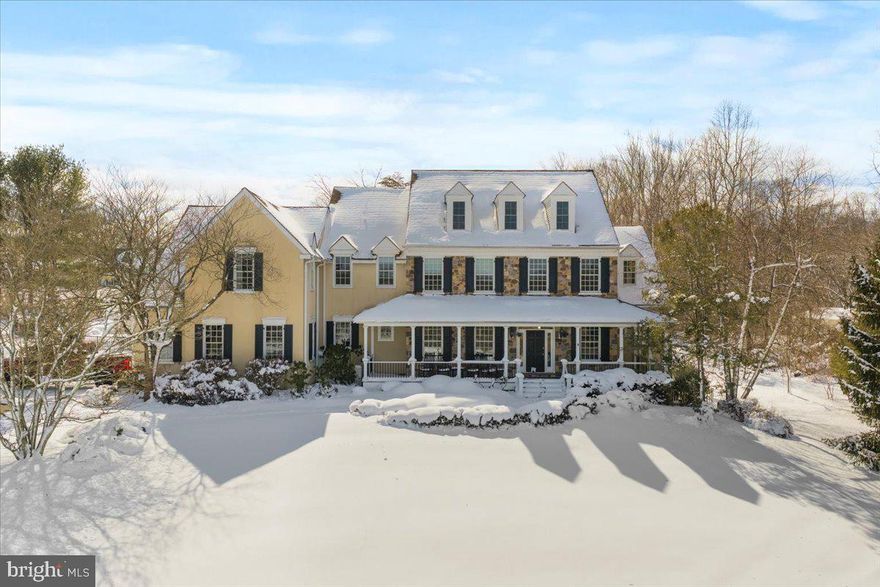 Welcome to this stunning Bucks County estate where timeless craftsmanship, natural beauty, and refined living converge on 5 breathtaking acres within the coveted Council Rock North school district. Set gracefully beyond a meadow of pollinators and framed by a wraparound porch, this custom masterpiece invites you to savor sunrise mornings overlooking your private landscape. Every detail has been thoughtfully curated to create a residence that is grand in scale and intimate in comfort. A soaring 2-story foyer with dramatic turned staircase, rich wainscoting, thick crown molding, arched hallways with keystones, and transom windows introduces interiors bathed in natural light. Hardwood floors flow throughout the main level, leading into a sophisticated formal living room adorned with a coffered ceiling and gas fireplace. French doors open to a serene deck echoing gentle sounds of the nearby Neshaminy Creek. The chef’s kitchen is nothing short of extraordinary, designed for culinary artistry and elegant entertaining. Granite counters, knotted pine cabinetry, Sub-Zero refrigerator, 48” gas range, pot filler, double ovens, wine refrigerator, stand mixer appliance lift, and an expansive island with butcher block carving station anchor the space. A tray ceiling breakfast room wrapped in windows provides the perfect setting for quiet gatherings. The great room impresses with its cathedral ceiling, wood-burning fireplace, and architectural trim, creating a warm yet dramatic space for connection. This wing of the home is enhanced by a walk-in pantry, coffee station or dry bar, well-appointed laundry room with folding station, powder room, and direct access to the oversized three-car garage. On the opposite wing, formal entertaining shines in the elegant dining room. An executive office with custom cherry cabinetry, an additional powder room, and walk-in closet contributes to sophistication and functionality. Upstairs, hardwood floors continue through the hallways accessed by both formal and casual staircases. The primary suite is a haven, featuring a tray ceiling, extended sitting area, vanity station, and dual walk-in closets. The spa-inspired bathroom boasts separate vanities, a soaking tub, private water closet, and an expansive shower with dual rain heads, all overlooking panoramic views of the estate grounds. A princess suite enjoys a spacious closet and its own private bath, while two additional bedrooms with walk-in closets share a thoughtfully designed Jack-and-Jill bath with separate private shower and toilet. A thoughtful loft area creates a designated homework zone or additional home office. The third-floor retreat is comprised of a wooden ceiling, dormer windows, generous closet space, and newer carpeting, offering versatility as a fifth bedroom, studio, or lounge. The walk-out daylight lower level is designed for unforgettable entertaining, with gas fireplace, recreation area for pool table and games, full bar with sink and refrigeration, and a spacious fitness room adjacent to a fourth full bath. The unfinished section features abundant storage. Outdoor living rivals a private resort. The saltwater gunite pool creates a focal point for summer gatherings, with waterfall and spacious integrated hot tub for up to twelve friends. A charming pool house includes a powder room, storage, and space for a future tiki bar or cabana lounge. At the rear of the property, a substantial pole barn with oversized doors, two deep garage bays, workshop space, and second-floor storage provides extraordinary utility for hobbyists or collectors. Newer roof (2017), HVAC system (2018), water heater (2023), robust 400-amp electrical service, and a partial house generator, ensuring peace of mind for years to come. Adjacent to preserved land, this extraordinary estate represents a rare opportunity to own a private sanctuary where luxury, land, and lifestyle align. Experience the estate that redefines elevated Bucks County living.