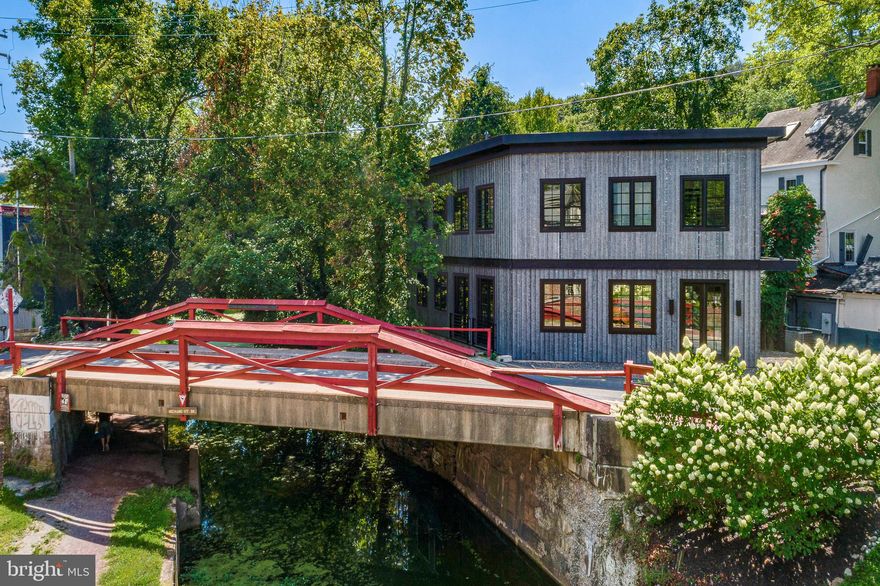 A rare opportunity invites you to own an architecturally brilliant home in the heart of New Hope, Pennsylvania. Perfectly situated on a charming canal street, this residence is naturally set apart from the lively Main Street by a tranquil canal. The signature red wooden bridge, one of New Hope’s most photographed landmarks, serves as your picturesque gateway to the town’s acclaimed restaurants, boutiques, and galleries. This newly constructed modern masterpiece showcases an inspired blend of European influence and contemporary design, drawing from Amsterdam and early modernist architecture. The interplay of light, space, and structure throughout its three levels creates a truly captivating living experience. Upon entering through the front entrance, a warm and inviting foyer welcomes you, with a striking staircase leading to the main living area. The open-concept design showcases gleaming hardwood floors and a refined sense of flow between each space. At the heart of the home is a beautifully designed wet bar with generous counter seating, perfect for entertaining. The living and dining areas exude modern sophistication, enhanced by expansive glass windows that fill the space with natural light. The sleek kitchen features black-grained European cabinetry, quartz countertops, a concealed pantry, and a substantial center island that anchors the room. Completing this level is an elegant billiard room with a custom built-in feature and a conveniently located powder room. On the second level, the full-floor owner’s suite offers the ultimate retreat with a spa-style bathroom, private terrace with a custom wet bar, office/study, laundry area, and a custom-upgraded closet system. Elegant window treatments, wallpaper accents, and designer lighting fixtures elevate each space with tailored sophistication. The lower level is equally impressive, featuring two additional bedroom suites each with its own full bath, a second laundry room, and a lounge area. Installed closets and upgraded storage systems enhance functionality and style. Every inch of the property has been thoughtfully curated, from the paver driveway and professionally landscaped grounds with lighting, to the artificial turf backyard overlooking the canal. Premium upgrades include a whole-house Generac generator, security and video system, triple sump pump system, whole-house carbon water filtration, an EV charger and a custom gutter system. Additional highlights include an elevator, three + private parking spaces, and direct canal access for a serene outdoor experience. With excellent proximity to both New York City and Philadelphia, you can enjoy New Hope’s vibrant lifestyle while living in your own private sanctuary. New Hope-Solebury School District is rated 10/10, and this address enjoys a premier in-town location surrounded by acclaimed dining such as Zoubi’s, Nektar, and Karla’s. Experience the best of luxury, design, and convenience, a home where every day feels like a holiday.