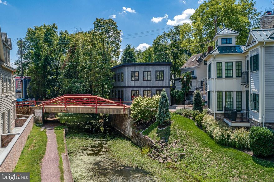 A rare opportunity invites you to own an architecturally brilliant home in the heart of New Hope, Pennsylvania. Perfectly situated on a charming canal street, this residence is naturally set apart from the lively Main Street by a tranquil canal. The signature red wooden bridge, one of New Hope’s most photographed landmarks, serves as your picturesque gateway to the town’s acclaimed restaurants, boutiques, and galleries. This newly constructed modern masterpiece showcases an inspired blend of European influence and contemporary design, drawing from Amsterdam and early modernist architecture. The interplay of light, space, and structure throughout its three levels creates a truly captivating living experience. Upon entering through the front entrance, a warm and inviting foyer welcomes you, with a striking staircase leading to the main living area. The open-concept design showcases gleaming hardwood floors and a refined sense of flow between each space. At the heart of the home is a beautifully designed wet bar with generous counter seating, perfect for entertaining. The living and dining areas exude modern sophistication, enhanced by expansive glass windows that fill the space with natural light. The sleek kitchen features black-grained European cabinetry, quartz countertops, a concealed pantry, and a substantial center island that anchors the room. Completing this level is an elegant billiard room with a custom built-in feature and a conveniently located powder room. On the second level, the full-floor owner’s suite offers the ultimate retreat with a spa-style bathroom, private terrace with a custom wet bar, office/study, laundry area, and a custom-upgraded closet system. Elegant window treatments, wallpaper accents, and designer lighting fixtures elevate each space with tailored sophistication. The lower level is equally impressive, featuring two additional bedroom suites each with its own full bath, a second laundry room, and a lounge area. Installed closets and upgraded storage systems enhance functionality and style. Every inch of the property has been thoughtfully curated, from the paver driveway and professionally landscaped grounds with lighting, to the artificial turf backyard overlooking the canal. Premium upgrades include a whole-house Generac generator, security and video system, triple sump pump system, whole-house carbon water filtration, an EV charger and a custom gutter system. Additional highlights include an elevator, three + private parking spaces, and direct canal access for a serene outdoor experience. With excellent proximity to both New York City and Philadelphia, you can enjoy New Hope’s vibrant lifestyle while living in your own private sanctuary. New Hope-Solebury School District is rated 10/10, and this address enjoys a premier in-town location surrounded by acclaimed dining such as Zoubi’s, Nektar, and Karla’s. Experience the best of luxury, design, and convenience, a home where every day feels like a holiday.