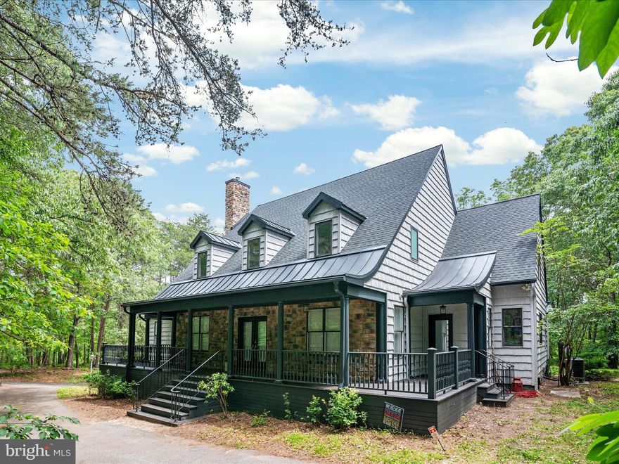 This large, spectacular waterfront home, with over 3,800 square feet of living space (and potential for more expansion within the home’s original footprint) somehow still manages to exude a charming “cottage in the woods” kind of feeling. The property extends over 6.03 partially wooded acres in the quiet North Shore community of Pasadena. It has shallow water frontage on Grays Creek with a 70-foot dock and water views from two sides. Originally built to classic Southern Living plans, this modern cottage has been completely re-imagined and thoughtfully renovated from top to bottom. The owners have created a beautifully modern, environmentally friendly, secure family estate. Upgrades are almost too numerous to list them all!

Hardwood floors extend to all three levels. The primary bedroom’s en suite bath was completely renovated and includes heated marble floors and a garden tub. The kitchen has new granite countertops and stainless steel Kitchen Aid appliances. The custom-designed hardwood staircase in the central corridor creates an elegant anchor to the main level. Upstairs, both bathrooms were renovated, including an extensive redesign of the hall bathroom.

Energy efficient and cozy pellet stoves add heat to the primary bedroom, the living room, and the garage/workshop. The pellet stoves provide backup heat on cold nights in addition to the central HVAC system and the geothermal heating and cooling systems. Foam insulation was added into the second floor walls and the attic. In the attic—a huge space with ample headroom—a new HVAC system was added. Thus the attic is now a conditioned, insulated space, already wired and ready to be converted to additional living space or provide climate-safe storage. The asphalt roof was fully replaced in 2022, with metal dormers added as well as metal sections where the roof profile curves towards the horizon, which will enhance the long-term waterproofing of the roof system.

The basement has two layers of 3/4” sheet rock for sound insulation, perfect for action-packed movie nights in the recently finished screening room. Just off the screening room is another space that was designated in the original plans to be a wine cellar. Three new heavily insulated garage doors were also added, as well as a dedicated power supply for whatever car charger a new buyer might wish to install. A large deck off the back of the house was rebuilt with underpinnings and storage underneath. The deck has views of the water and woods, as well as a hot tub. The owners also completely redesigned and replaced the front porch to create one big, elegant wraparound porch.

The owners enjoy a water doctor water system that purifies water with no chemicals (replacing the original chemical-based system), as well as a redundant reverse osmosis system for drinking water. An open lawn behind the house was originally slated for a detached three-gar garage with a second-story living space. The current three-car garage and workshop had originally been conceived as a 1100-square-foot au pair suite.

Six security light poles and 54 cameras provide significant security around the property. They also provide six sets of outdoor outlets and, to keep it fun, each pole is equipped with an outdoor sound system! Perfect for summer parties, the music extends all the way to the 400-square-foot outdoor dance floor next to the dock! The dance floor was refreshed this spring with drainage improvements and fresh paint. The 70-foot dock provides perfect water access for canoes, kayaks, SUPS and catamarans. It also offers priceless views of the birds, fish and shoreline of this slice of paradise on Gray’s Creek.

The voluntary North Shore neighborhood association includes access to a private marina and boat ramp and a community beach. It is rare to find a property like this, one that has been massively upgraded and improved from its original plans, and yet still has so many more possibilities for future plans and generations.