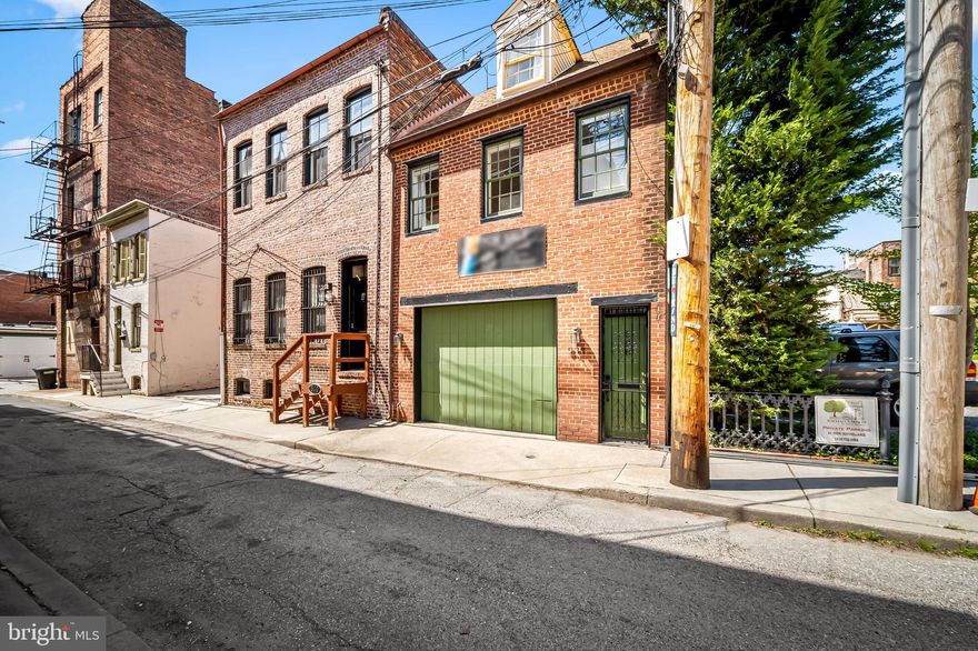 Rare Find in Ridgely’s Delight: Updated End-Unit Rowhome with Garage & Private Garden

Discover a true gem tucked away on a quiet side street in the heart of Historic Ridgely’s Delight. Originally a 19th-century carriage house, this unique home sits adjacent to a magnificent 1780s residence (now a charming Inn), offering a rare connection to Baltimore’s deep history. Combining period character with tasteful modern updates, this end-of-group rowhome is a tranquil retreat just blocks from UMMC and Camden Yards, and within easy walking distance to the Inner Harbor.
The main living space on the second floor is designed for efficient urban living with hardwood flooring throughout. This compact heart of the home features an open-concept kitchen with a breakfast bar and stainless steel appliances that flows directly into an inviting living area, accented by a stunning original brick feature wall. This level also includes a serene bedroom anchored by a striking floor-to-ceiling exposed brick wall, located adjacent to a fully updated, well-designed bathroom.
The third floor consists of a large open loft space. Featuring a cathedral ceiling and cooling ceiling fan, this flexible area is ideal for use as a primary suite, a spacious home office, or an inviting guest retreat.
The ground level is anchored by a versatile 13' x 20' garage, recently upgraded with a new door and video monitoring system. This space offers incredible flexibility: use it for secure parking or transform it into a private workout studio or a "party space" for game-day gatherings. This level also includes a dedicated laundry room and extra storage for added convenience.
Just outside, the private garden has been thoughtfully landscaped to include a patio made of reclaimed local bricks and raised garden beds filled with easy-care native plants. When in full bloom, the garden offers a lush, fragrant escape from the bustle of the city.
This home is as functional as it is beautiful and can be sold partially furnished for a seamless move-in experience.