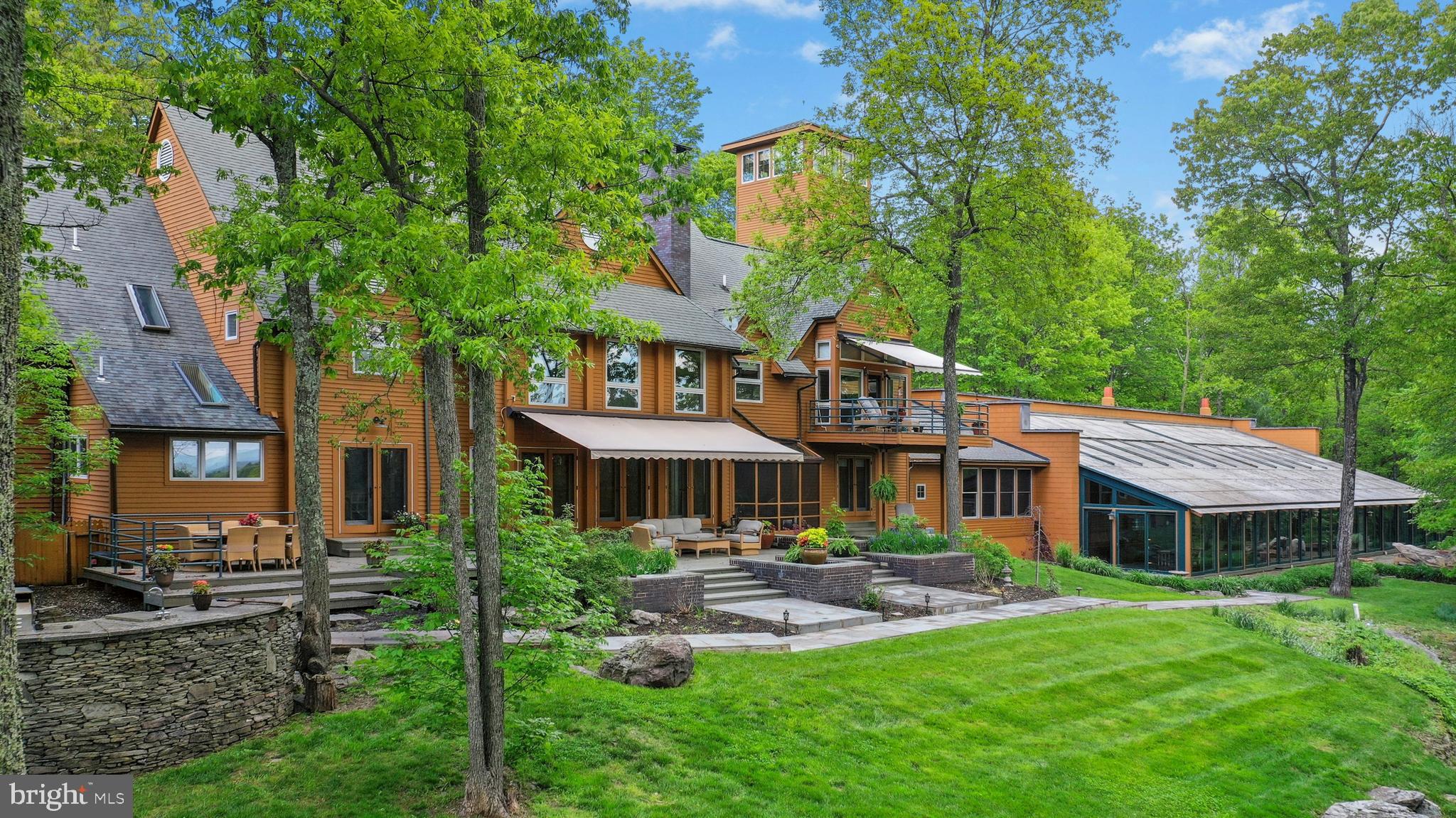 Just minutes from major commuter interstates, a country road in the heart of the beautiful Pocono Mountains winds through lush countryside to a gate that doesn’t offer even a hint of what is found beyond. If you are lucky enough to be granted entrance, the drive sweeps past boulders and around bends to a stunning mountaintop lodge centered on 73 acres, a backdrop befitting a James Bond movie.
Inspired by the beauty and magnitude of its surroundings this remarkable 13,000 square foot residence showcases all the fine materials and craftsmanship of an earlier age coupled with the drama, efficiency and conveniences of modern construction, all finely curated and meticulously maintained. Rare and unusual design elements welcome you to the lodge with an open dining room that will amply accommodate large gatherings and is appointed with Ironwood trees, natural flagstone floor and wall of windows. The voluminous great room was designed with extreme care to blend its strong architectural character and exceptional detailing into a dramatic and comfortable space punctuated by its cathedral ceiling, floor-to-ceiling brick fireplace, African rosewood floors and walls of windows to embrace the sun in the winter and the sun-dappled views in the summer. A thoughtfully planned kitchen, with high-end appliances and amenities to please the most discerning of cooks, opens to a large patio with outdoor kitchen, inviting al fresco dining.
There should be no need to leave the compound for entertainment. The lodge offers an acoustically engineered media room, sunken bar room with fully outfitted marble bar, library and a commercial gym. The star of the recreation options is the indoor saltwater pool and spa complete with desert air system. Here heated flagstone floors and walls of glass doors frame the pool and invite one to swim while the snow flies. Refreshments will be served from the poolside bar and the unique open hearth propane fireplace will enhance the ambiance. Dual bathrooms are conveniently located steps away.
The second floor primary suite is a sanctuary that draws you through glass doors onto the private balcony to take in the distant mountains with no signs of civilization in view. Here every amenity is elegantly embraced in the adjacent sitting area with fireplace, bedroom area with cathedral ceilings and retractable projection screen. The ensuite bath offers marble steam shower, whirlpool tub and marble vanity. Dual closets and a dressing area with handsome built-ins will amply accommodate your wardrobe. In addition to the primary suite five additional bedrooms, including two main-floor bedroom suites, will offer sanctuary to friends and family.
An observation tower rises 40 ft above the main floor to its pinnacle on the fourth level, the perfect place to leave the world behind, savor the quiet and be eye level with soaring hawks and rainbows cresting the mountain.
Comfort is ensured by a commercial whole-property generator, intricate heating and cooling systems and high-tech security system. A historic c.1700s barn was carefully disassembled from its original location and reassembled on the property to provide garaging for 12+ cars and collections. Heated floors, insulated walls and ceilings, remote controlled sliding doors, washer and dryer and separate security system provides enviable workspace.
The Pocono Mountains with its four seasons of natural beauty, clear lakes and rivers, luxurious resorts and colorful festivals, has been a beloved vacation destination for generations. When you need to leave this extraordinary oasis you will be delighted to know that grocery stores, restaurants, resorts and ski slopes are a hassle-free 15 minutes drive. New York City is a world away, but can be easily accessed in two hours via Interstate Route 80.