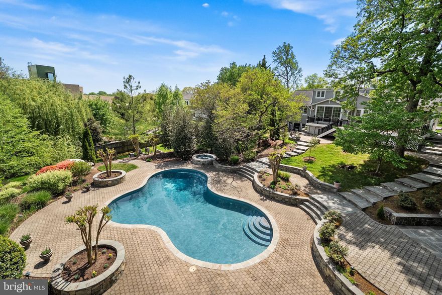 Tucked away on nearly one acre of lush, mature landscaping, this remarkable residence offers a quiet, peaceful lifestyle that feels worlds away from the city—yet is only minutes to Old Town Alexandria and Downtown Washington, DC. The setting evokes the calm and privacy of the countryside, where gardens, stone paths, and open skies create a sense of retreat, while daily conveniences, dining, and cultural destinations remain effortlessly close.

The home spans nearly 4,300 finished square feet across three thoughtfully designed levels, offering three to four bedrooms, a private office, three full baths, and one half bath. The primary suite is conveniently located on the main level, providing ease of living and a seamless connection to the home’s outdoor spaces.

Mature gardens, layered stonework, and manicured grounds frame a resort-style, heated saltwater pool, fully refreshed with new gunite and equipment in 2023. This inviting centerpiece is complemented by an extraordinary outdoor pavilion that rivals a premier entertainment venue. Designed for year-round use, the pavilion features dual built-in grills—including a natural gas Bull BBQ with infrared burner and a Santa Maria Argentine charcoal grill—along with a fireplace, integrated storage, infrared heaters, ceiling fans, and outdoor speakers, making it ideal for both intimate evenings and large-scale gatherings.

Inside, the residence reflects enduring quality and thoughtful investment throughout. Handcrafted alderwood cabinetry, radiant heated floors in the primary baths and guest suite, skylights with remote-controlled shades, whole-house water filtration, and advanced smart-home systems enhance comfort and livability. Premium appliances by Sub-Zero, Dacor, and Miele support everyday living and effortless entertaining. An EV charger, upgraded roofing, modern mechanical systems, and comprehensive security further underscore the home’s turnkey appeal.

From the Ipe decking and Belgian cobblestone driveway to the serene gardens and stone terraces, every detail has been curated with longevity, function, and beauty in mind. This is a rare offering: a private, country-like retreat with the scale and amenities of a luxury estate—exceptionally close to the energy and sophistication of Old Town and Washington, DC.