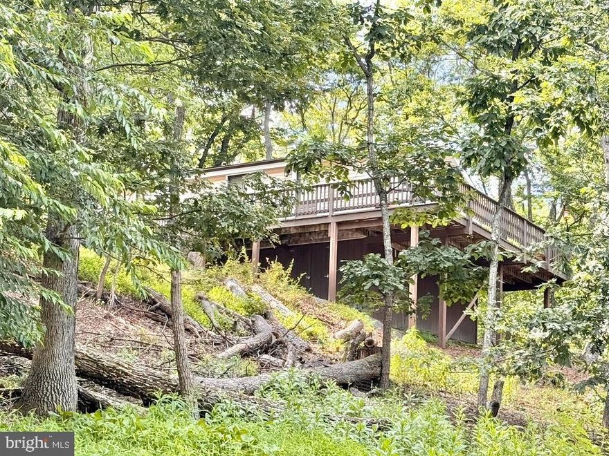 117 Tuckahoe Trail is not just a cabin—it’s a creative escape, a peaceful home base, and a direct invitation into the wild.  Come see what it feels like to live in a place where the forest is your backyard and every  corner tells a story. This property is being sold strictly AS-IS.

117 Tuckahoe Trail is truly a one-of-a-kind mountain retreat. Perched high on a wooded ridge in the beloved  Woods community of Hedgesville, West Virginia, you will find a property that feels more like a storybook hideaway than just a cabin.  With hand-built artistry, curated natural spaces, and direct access to one of the state’s largest wildlife preserves, this soulfully designed home is a rare opportunity to live surrounded by peace, purpose, and nature.

Step inside and feel the warmth of a thoughtfully crafted 2-bedroom, 1-bath layout, wrapped in natural wood tones and vaulted ceilings with exposed beams. The central living space is anchored by a charming wood-burning stove and framed by a wall of windows that looks out into the treetops. In cooler seasons, you’ll enjoy seasonal mountain views stretching across the ridge as the leaves drop. The atmosphere is both serene and creatively energizing—perfect for quiet mornings, artistic afternoons, and fireside evenings.

The kitchen pairs solid wood cabinetry with open shelving and a colorful, vintage, stained-glass pendant light, maintaining the home's handcrafted feel. The bathroom was substantially renovated in 2025, now featuring a designer wood-slat vanity, updated sink and faucet, modern mirror, new lighting, and stylish finishes. Two cozy bedrooms provide space to sleep or work, and a rustic built-in ladder leads to a loft above—ideal for extra storage or sleeping space.

In 2017,   LVP flooring installed throughout and the water heater was replaced and professionally relocated to the crawl space to optimize the interior layout. A stacked washer and dryer was also installed, making day-to-day living easy without compromising the home’s charm. Two new window HVAC units were installed in 2025 for seasonal comfort. The systems are simple, reliable, and well maintained.

The magic continues outside. From the expansive front deck, you’ll feel as though you're sitting in a treehouse. Look closely and you’ll notice small works of art all around—sculptures of deer and chairs built from sticks and logs found on the land itself. A black garden gate opens into a stone-bordered garden and hand-built raised beds crafted from stacked logs. Everything here tells a story of care and creativity.

In 2002, a 420 sq ft detached garage and heated, insulated workspace were added to the property—perfect for woodworking, gardening, gear storage, or creating your next masterpiece. Likely during the same year, the roof and siding were updated, contributing to the cabin’s solid and polished presentation. The workshop features full wall built-in pantry-style shelving from floor to ceiling.

What makes this property so exceptional is its location: it literally backs up to Sleepy Creek Wildlife Management Area, a sprawling 22,928-acre protected forest that offers hiking, mountain biking, foraging, fishing, camping, and regulated hunting (with a WV license). You'll find trail access just beyond your yard, as if nature is welcoming you in. 

The home sits inside The Woods subdivision—a well-maintained mountain community known for its privacy, quiet roads, and year-round living. While this property does not include a Woods Club membership, reactivation of a previous membership may be possible (buyer to confirm directly with the Club). The golf course is open to the public, and HOA dues include trash removal, road maintenance, and snow removal and an onsite community office with a full-time manager.