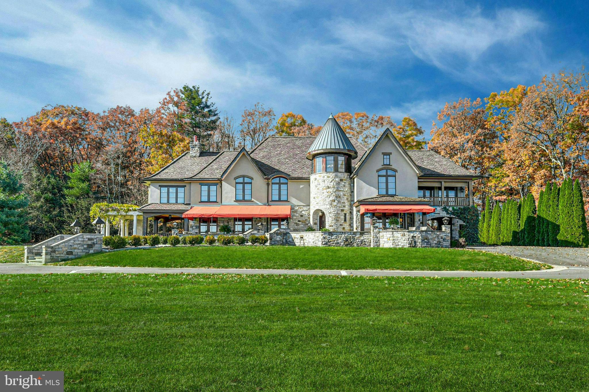 Polished, with understated notes of elegant, crisp, and luxurious, this custom crafted Tudor home and vineyard known as Tutto Niente is a master class in creating the perfect blend. The quarter mile driveway winds through tall trees before rounding a corner to reveal a stunning panoramic view over 55 acres of big sky and Pocono Mountains. Designed and crafted as the family home, the owner/builders did much of the work themselves using materials sourced from the land whenever possible. Custom millwork, unique decorative paint treatments, textured walls, and magnificent lighting are just a few of the hallmarks throughout. Every room of the house features radiant heat floors for year round comfort. Guests enter through a round entryway foyer which opens in turn to the vast 2-story great room with a massive Indian granite fireplace. Nearby is the media room, with a floating oak ceiling and velvet walls, and a spacious dining room with domed gold-leaf ceiling. The newly renovated extensive modern kitchen will impress even the most discriminating of chefs with 2 quartz islands, high end Viking and Thermador appliances and a spacious cocktail wine bar area perfect for entertaining. A step down leads to the cozy family room, with a gas fireplace and curved mahogany wall with floor-to-ceiling windows and doors looking out over the vineyard. The main staircase, inspired first by the Governor’s Mansion in Connecticut and then renovated with inspiration from the 1920s Empire Hotel in Manhattan, is custom crafted with mahogany newel posts and steel balusters with brass accents. Upstairs, the primary suite is a feast for the senses upon entering the warm and spacious sitting room with gas fireplace. A reclaimed glass wall serves as a room divider to the bedroom with a barrel ceiling painted in a shimmering harlequin pattern and a private balcony, and a 3-part bath with soaking tub nestled within the turret. A recently renovated guest suite is on this level, as well as a third suite and two large bedrooms that share an additional recently renovated hall bath. The finished lower level includes a kitchenette, recreation room, den and full bath. This thoughtfully designed, custom built home overlooks a beautifully tended vineyard and is surrounded by extensive acreage, long-range vistas, and inspiring sunrises that change daily with each season. Raise a glass to the elegance of Tutto Niente!