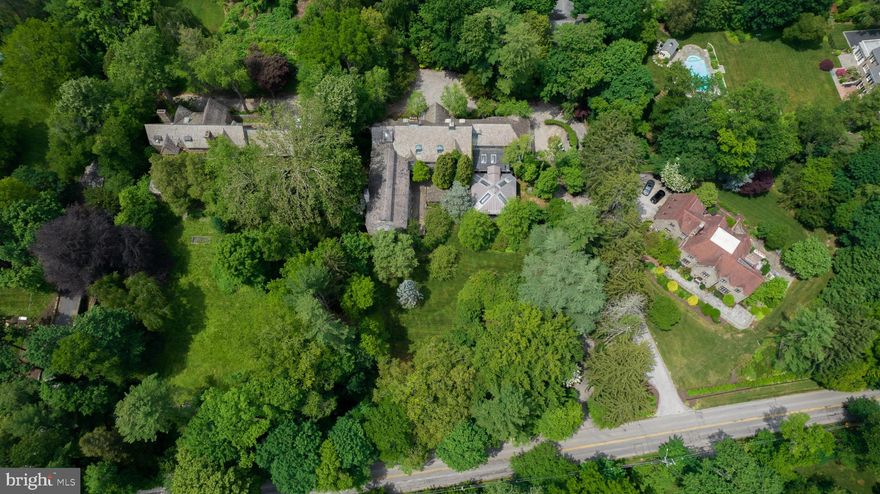 This grand stone manor home is situated on over 1.5 fabulous acres of land offers a prime opportunity to put your own personal stamp on an incredible piece of history and architecture. The main house approached from Grays Lane is distinctive and expansive, brimming with beautiful wood detailing and other fabulous features like s slate roof, an arch from the 14th century; French stained glass from the 18th century; 5 wood-burning fireplaces including one in the great room hand-carved in the late 1600s; stained glass accents; intricate moldings and millwork; vaulted wood beam ceilings; a striking staircase with 18th century ironwork railing rising to a library; an indoor pool with 4 skylights; and a built-in aquarium in one of the bedrooms! This exceptional residence is built for entertaining and boasts incredible spaces for formal gatherings. Think of The Great Gatsby! A grand living room/great room and banquet-sized dining room can accommodate huge gatherings of 80+ guests. Sets of French doors open to the wonderful flagstone terrace where you can dine alfresco, host cocktail parties, and enjoy the lovely setting. The large new kitchen featuring a huge hand-carved island by Winterthur Artisans, an indoor brick grill, stainless steel appliances and a butlers pantry is ideal for cooking meals and catering events. Generous bedrooms include several private suites and provide versatile sleeping quarters for family, guests and staff. Plus there are 4 full baths and 4 powder rooms spanning the 3 levels. Heightening the allure are 2 home offices with built-ins, 2 libraries with handsome bookcases, abundant closet and storage space, main and rear staircases, 2 laundry facilities, and a 3 bed 2 full bath apartment with kitchen above garage, accessed by several entry points from inside and outside the house. Here is your chance to own a piece of history, build a legacy, and personalize a luxury oasis on sprawling grounds in a premier neighborhood.