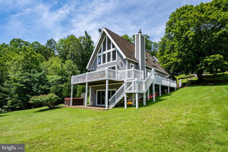 Lakefront Chalet at Deep Creek Lake - Minutes from Wisp with deeded single-slip dock, this chalet pairs precision and polish. Vaulted ceilings crown a sunlit open plan with tongue-and-groove accents and a stacked stone fireplace. Sleek and clean kitchen with stone counters, stainless appliances, and hardwood cabinetry. A finished walkout basement adds lounge and rec space. Upstairs loft hosts the primary suite overlooking two levels of glass framing panoramic lake views. Wraparound deck with two stories of outdoor living complete with a hot tub. New roof. Level yard. Private, sharp, and ready for your future lake life... Call today for private showing! **New roof being installed, scheduled to be completed Friday, 7/25.