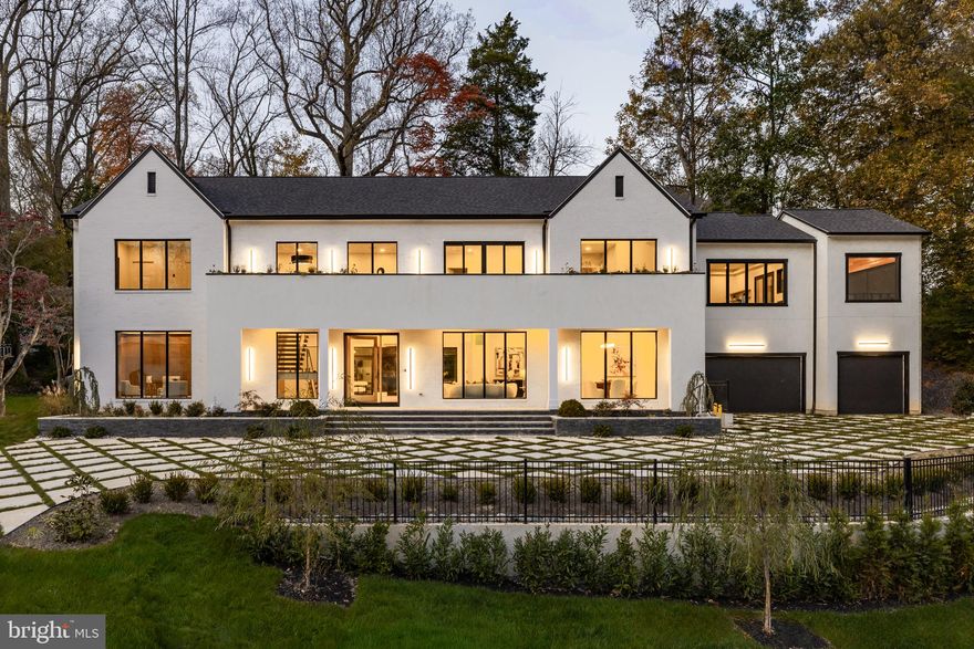 Tucked within a serene cul-de-sac in Bethesda’s coveted Burning Tree neighborhood, 6605 Lybrook Court represents the latest collaboration between renowned builder Dena House and AP Architects. Recently completed on over half an acre, this custom contemporary residence spans more than 9,000 square feet across three thoughtfully designed levels, offering a rare combination of modern sophistication, enduring craftsmanship, and flexible living spaces.

Defined by clean geometry and finely curated materials, the home balances sleek modern elegance with lasting comfort. The striking façade, composed of Shouldice dimensional stone and white concrete and accented by black-clad Pella windows, is approached via a custom concrete block driveway with grass in between, providing parking for up to nine cars. A dramatic 25-foot-wide staircase leads to a 300-square-foot covered terrace with a luxury mahogany ceiling, framing the glass pivot front door and soaring double-height foyer.

Inside, a floating Viewrail staircase with four-inch treads and glass railings ascends before a 21-foot paneled red oak wall, creating the home’s architectural centerpiece. Expansive sightlines and abundant natural light connect formal and informal spaces seamlessly. The formal living and dining rooms flow effortlessly, while a distinguished study with custom millwork, dual built-in libraries, red oak–paneled walls, and a private exterior entrance provides an elegant and functional space for work or reflection.

The informal living area centers on a family room anchored by a striking gas fireplace within a porcelain and marble surround, framed by panoramic views of the rear terrace. Throughout the main level, 7.5-inch white oak floors, Visual Comfort lighting, and Lutron smart controls create a cohesive atmosphere of sophistication. The home is equipped with Bose and Polk sound systems, with 11 speaker pairs delivering immersive audio throughout.

The kitchen is both a statement and a sanctuary, featuring two-tone Wood-Mode cabinetry, Calacatta Silver quartzite surfaces, a waterfall island, a custom hood, and a full Wolf/Sub-Zero appliance suite. A butler’s pantry and walk-in secondary pantry provide abundant storage and prep space. A mudroom connects to the three-car garage and family powder room, while a main-level guest suite enhances multigenerational flexibility.

Upstairs, the primary suite is a retreat of exceptional comfort, with poplar-beamed ceilings, red oak paneling, dual custom walk-in dressing rooms (one with a Taj Mahal-topped island), and a private sitting room with kitchenette opening to a screened porch with a mahogany ceiling. The spa-inspired bath features a Negresco leather granite double vanity, Tappeti marble, Badeloft soaking tub, and expansive glass shower. Three additional bedrooms, each with ensuite baths and custom walk-in closets, surround a loft sitting area, with a conveniently located laundry room.

The lower level is devoted to recreation and relaxation, featuring a home cinema with 6.1 surround sound, glass-enclosed wine room, fully equipped bar and kitchenette, fitness center, and guest suite with full bath. A Savaria Eclipse elevator provides seamless access to all three levels.

Outdoors, two metal pergolas define distinct gathering areas, one anchored by a natural gas fire table. Custom concrete hardscaping and lush landscaping create a private, serene setting ideal for intimate dining or larger entertaining. Smart home systems, including Ring security, Nest thermostats, and WiFi-enabled appliances, integrate convenience and efficiency into daily life.

With meticulous craftsmanship, modern design, and a premier location blending tranquility with proximity to downtown Bethesda, 6605 Lybrook Court offers a rare opportunity to own a newly built residence of architectural distinction, where every detail reflects comfort, style, and timeless sophistication.