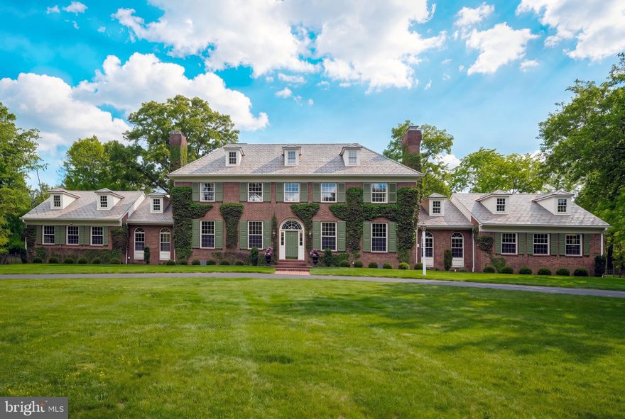 Prominently positioned on over 10 picturesque acres in sought-after Upper Makefield Township, 4 Woodland Road is a stately all-brick Georgian Colonial approached by a sweeping governor’s driveway and inspired by the timeless elegance of plantation-style architecture. Surrounded by serene natural beauty, this exceptional estate offers refined luxury, sophisticated design, and modern comfort throughout.
A dramatic two-story foyer welcomes you with a stunning butterfly staircase, elegant black-and-white checkerboard marble flooring, and access to the formal Living and Dining Rooms. Recently updated with a tasteful designer palette and thoughtful enhancements, the home showcases exquisite craftsmanship including decorative moldings, soaring ceilings, custom built-ins, four fireplaces, and Baldwin hardware throughout. The gourmet Kitchen is both warm and impressive, featuring a walk-in brick wood-burning fireplace, beadboard coffered ceiling, granite countertops, Viking cooktop, beverage refrigerator, chic pendant lighting, and direct access to the bluestone terrace for seamless indoor/outdoor entertaining. The adjacent Gathering Room is highlighted by a striking brick fireplace and a dramatic wall of arched transom windows overlooking the grounds. Additional main-level living spaces include a cozy Sitting Room with floor-to-ceiling custom built-ins, a spacious private Study with adjoining bonus room/playroom, and a gracious guest wing complete with two bedrooms, full bath, and private entrance — ideal for extended family or visitors. Upstairs, the centrally located Primary Suite serves as a luxurious retreat featuring dual spa-inspired baths, professionally organized walk-in closets, and tranquil property views. Two additional ensuite bedrooms with Juliette balconies overlooking the foyer complete the upper level. The finished lower level offers exceptional entertaining and wellness amenities including wide-plank wood flooring, wood-paneled ceilings, a stunning stone wine cellar with slate flooring, gym, sauna, full bath, and abundant storage.
Backing to mature woods, the private outdoor oasis features a sparkling in-ground pool and expansive bluestone terrace with ample space for lounging, dining, and entertaining. Additional highlights include:
Spacious mudroom 3-car garage, Newer  HVAC systems, Newer bedroom carpeting, Dog shower
Outdoor speaker system. Ideally located just minutes from downtown Newtown and New Hope, with convenient access to I-295, this extraordinary estate is situated within the highly acclaimed Council Rock School District and offers an exceptional blend of privacy, elegance, and convenience.