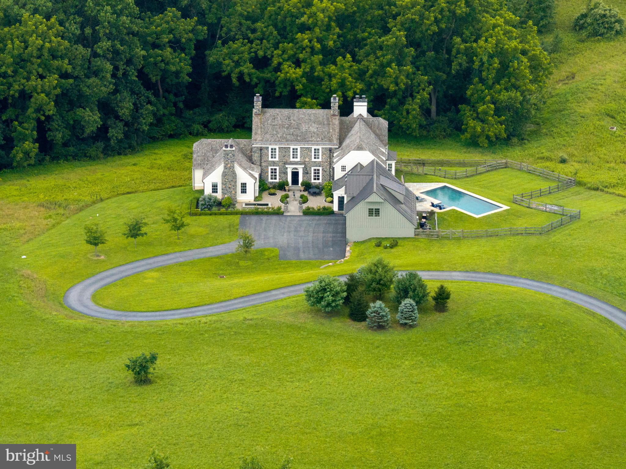 NEW PRICE! Stag & Thistle Farm is an extraordinary English Manor Country Estate set on over 44 acres, conveniently located just outside the picturesque village of Marshalton, which boasts the Marshalton Inn and Four Dogs Tavern. A gated entrance and a meandering drive usher you to this ideally placed residence, designed by Period Architecture and built by luxury builder Porter Construction in 2018. It beautifully blends centuries-old charm with the efficiency and modern conveniences of the 21st century. Nestled within the natural contours of rolling hills, this spacious home spans over 8,000 square feet and includes the potential for further expansion with an unfinished lower level of an additional 5,000 square feet. The entryway to this Stone Manor Home is via a lovely courtyard featuring a fountain and perennial gardens that provide vibrant color from early spring until fall. This grand yet inviting residence showcases timber trusses, plaster finishes, custom millwork, a groin ceiling, and various other exquisite elements. To the right, through custom-crafted arched doorways, lies an expansive gourmet kitchen featuring a breakfast nook that offers sweeping views of the rolling hills and countryside, an in-ground heated saltwater pool surrounded by elegant hardscaping, and stunning vistas of a 3-acre vineyard. This luxurious kitchen is equipped with top-tier appliances, a Tadelakt backsplash, soapstone countertops, a limestone-framed fireplace, an 8-burner range, and a Wolf Oven. The arched doorways lead into the family room, which boasts a vaulted ceiling, timber trusses, and a cozy wood-burning fireplace. The residence is awash with abundant natural light. The kitchen also has pocket doors that open into a spacious dining area, adorned with exquisite moldings. Nestled in its own private wing on the first floor, the primary suite features a vaulted ceiling, a fireplace, a lavish primary bath, and an adjoining laundry area. The first floor also includes an office with a fireplace that overlooks the woodlands. On the second floor, you will find three en-suite bedrooms along with an additional family room. A convenient mudroom, complete with a dedicated dog wash, provides access to a breezeway. Large stacking doors to the pool area on one side and the courtyard on the other. The breezeway also gives access to the garage and second floor art studio. Enjoy unparalleled views of the countryside from every room. Easy access and a 7-minute drive to West Chester, Kennett Square and Downingtown. 35-minute drive to King of Prussia, 50 minutes to Philadelphia, 2 hours to New York and 2 ½ to Washington, DC.